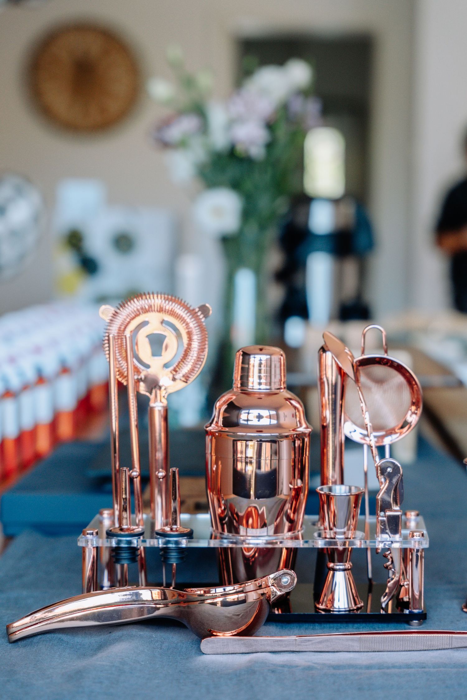 Collection of copper and stainless steel bar tools and cocktail equipment arranged on a blue surface.