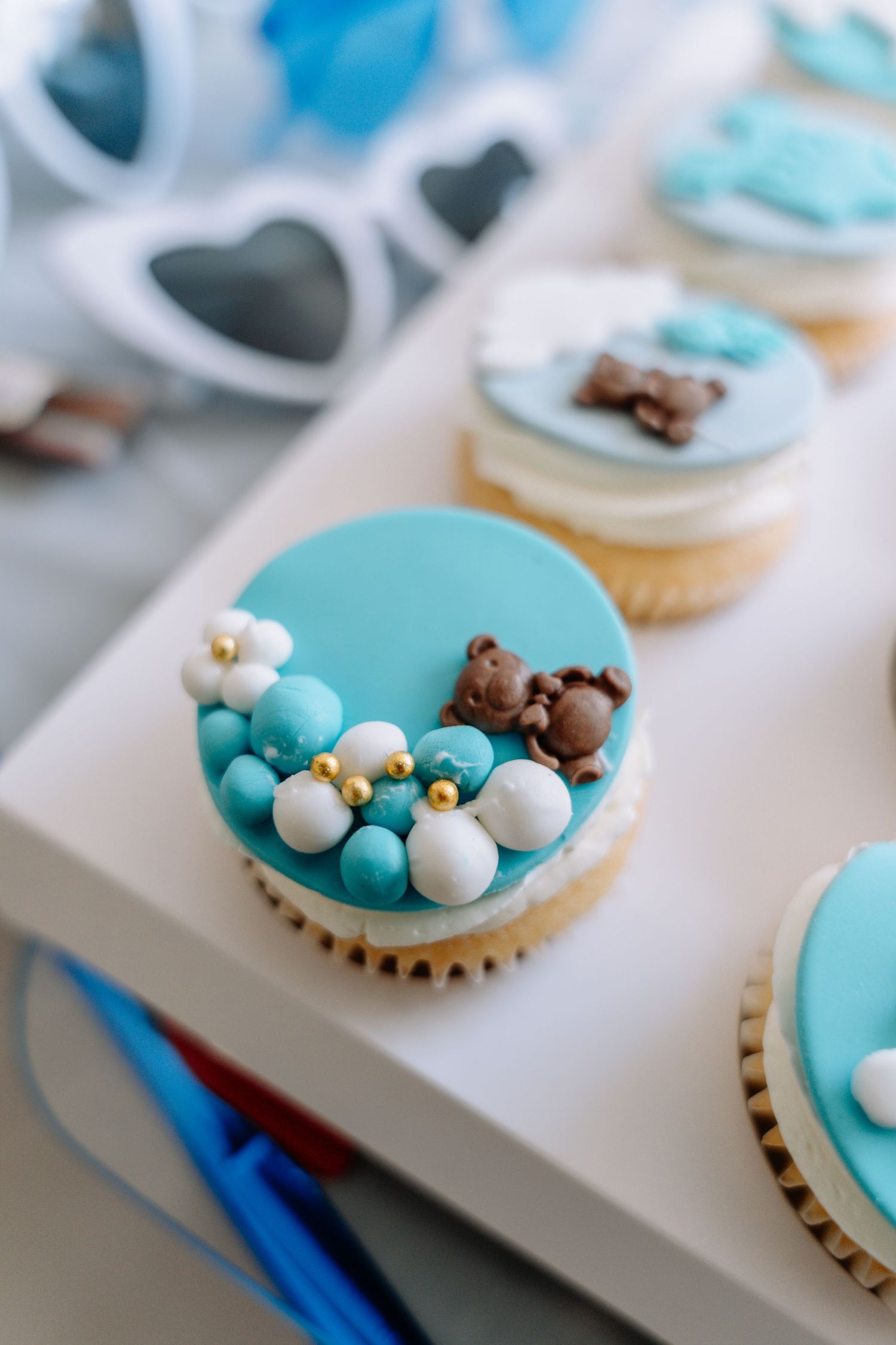 Close-up progression of decorating blue and white frosted cupcakes with pearl-like candy decorations.