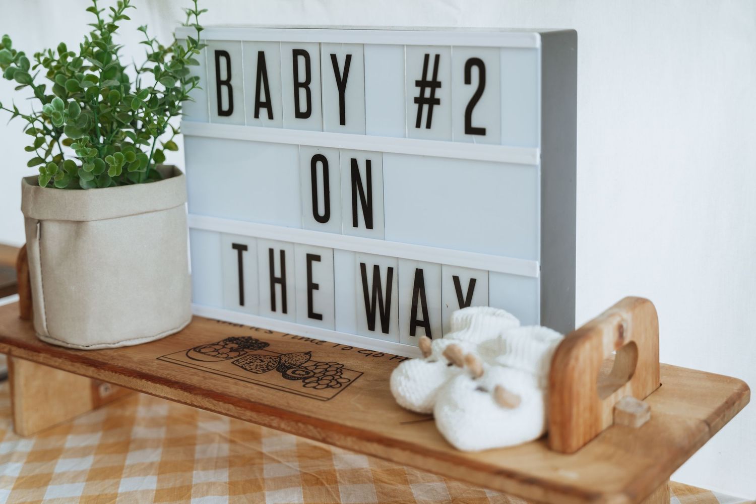 White letterboard sign with text 'BABY #2' displayed on a wooden surface with decorative elements.