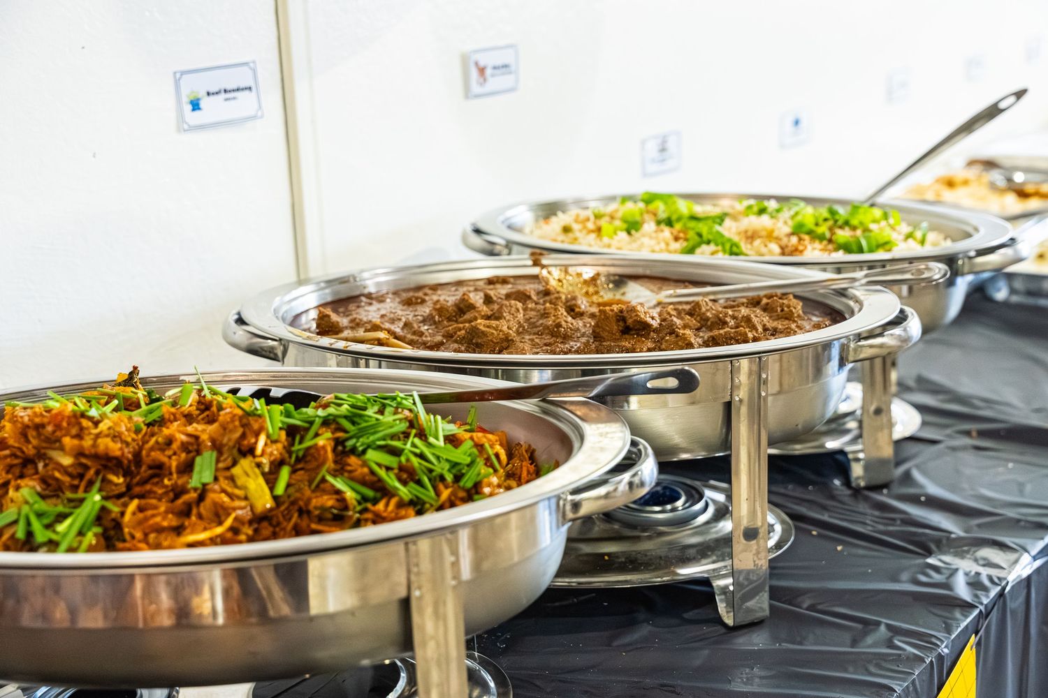 A buffet line with multiple stainless steel chafing dishes filled with various hot dishes and salads on a black tablecloth.