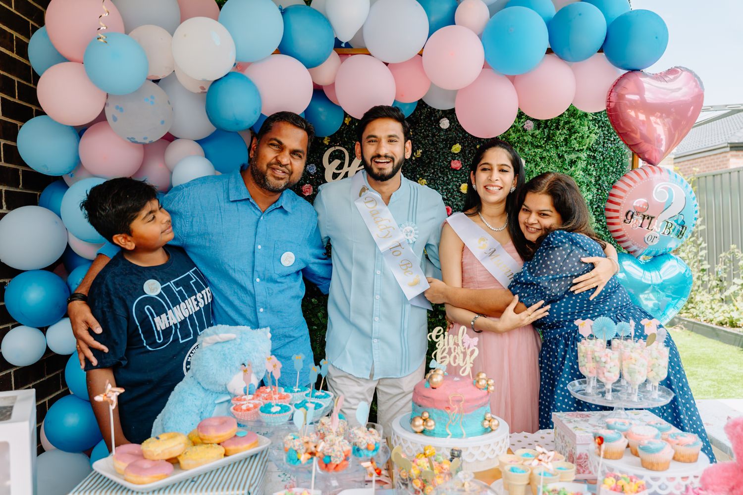 Gender reveal party setup with pink and blue balloon decorations and dessert table.