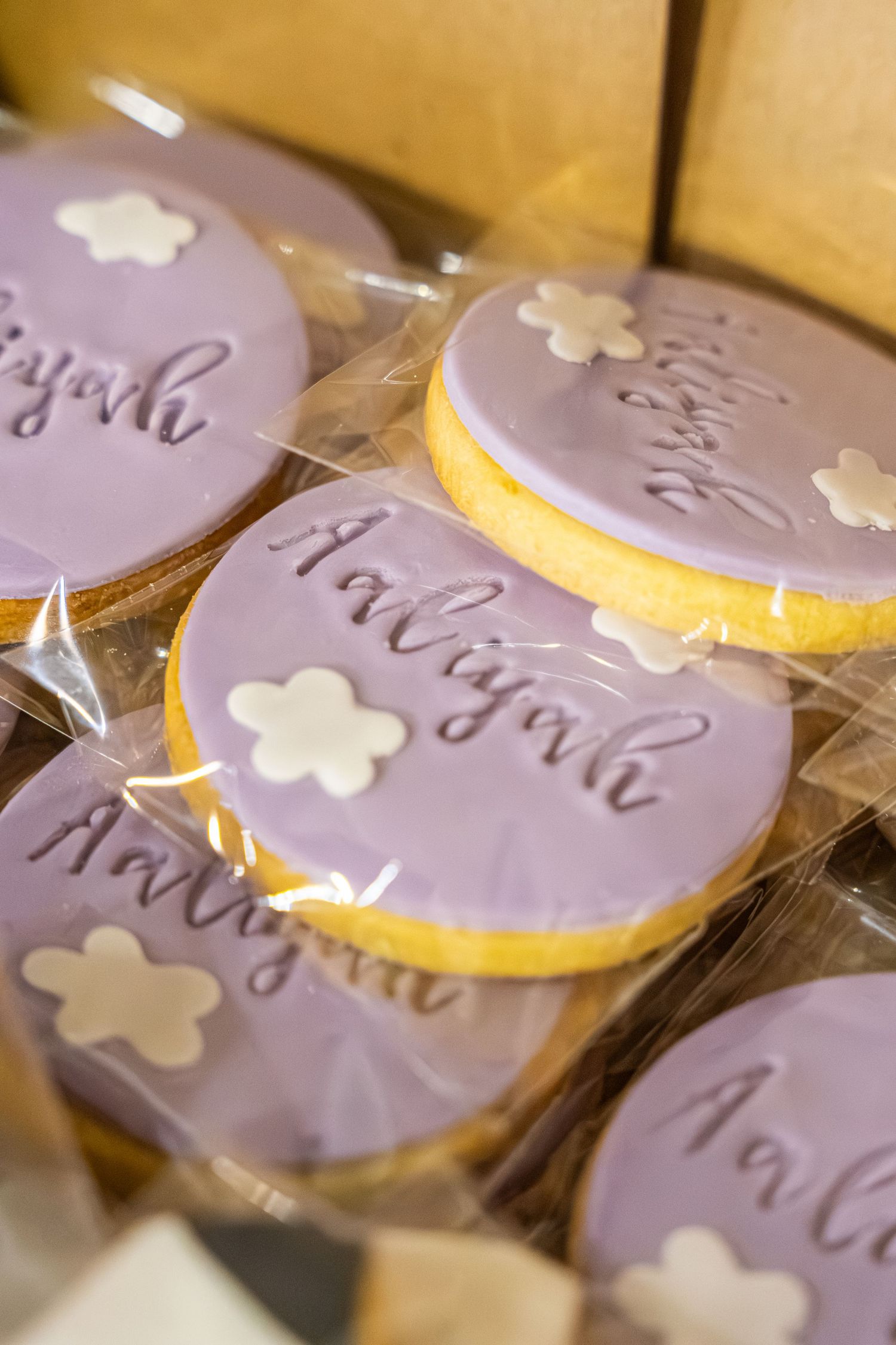 Purple frosted sugar cookies with delicate white flower decorations and elegant script writing arranged in neat rows.