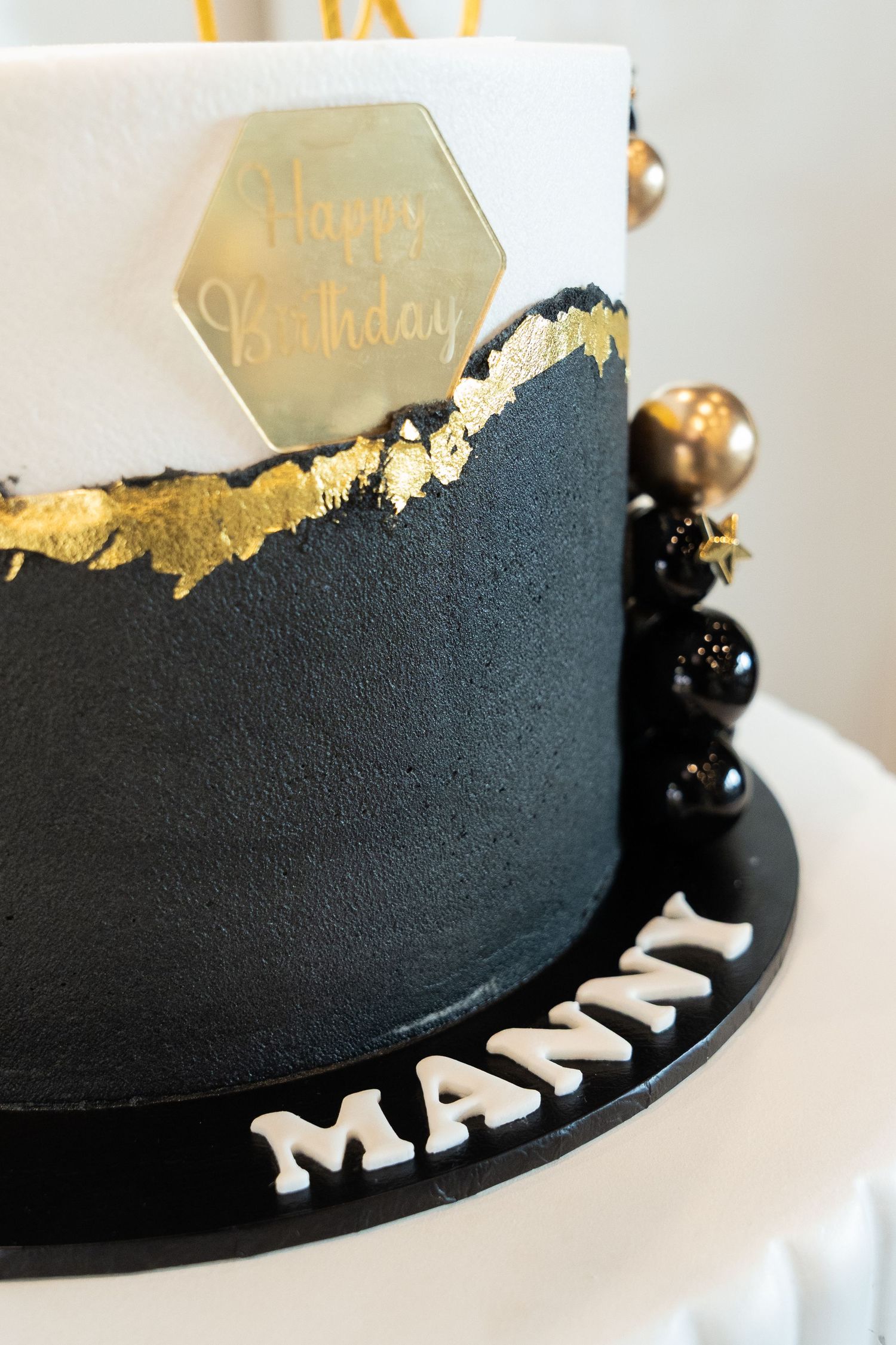 Close-up details of a black and gold birthday cake with elegant metallic accents and white lettering decoration.