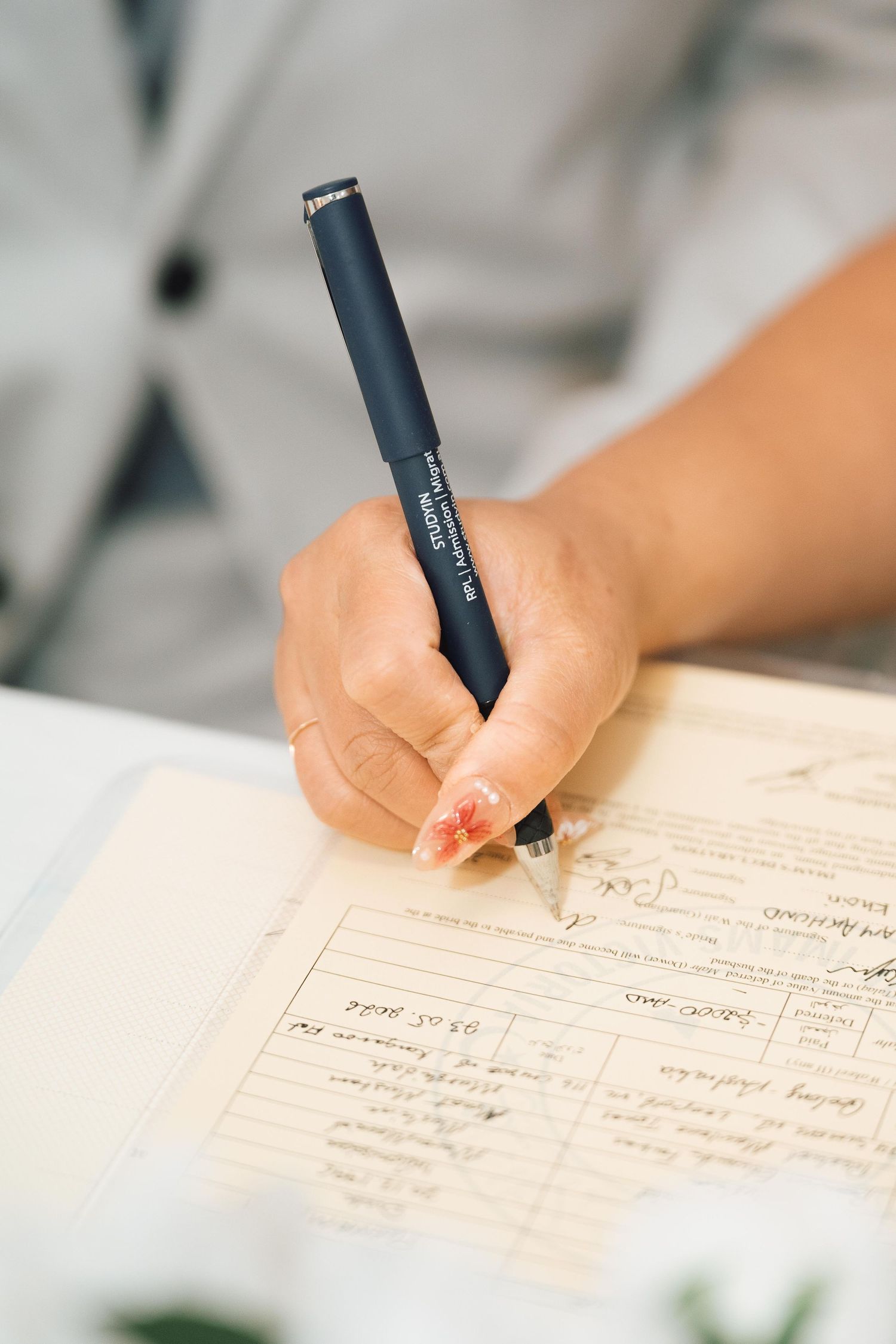 Close-up of a hand signing an official document with a dark blue pen, wearing a light gray blazer.