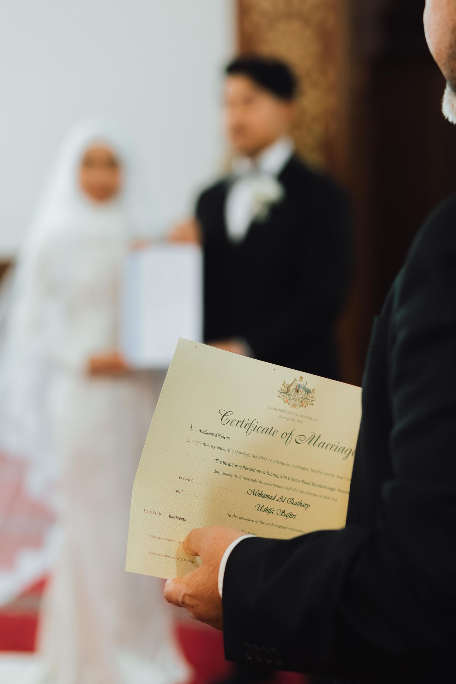Official holding a Certificate of Marriage with Muslim bride and groom standing in background during wedding ceremony.