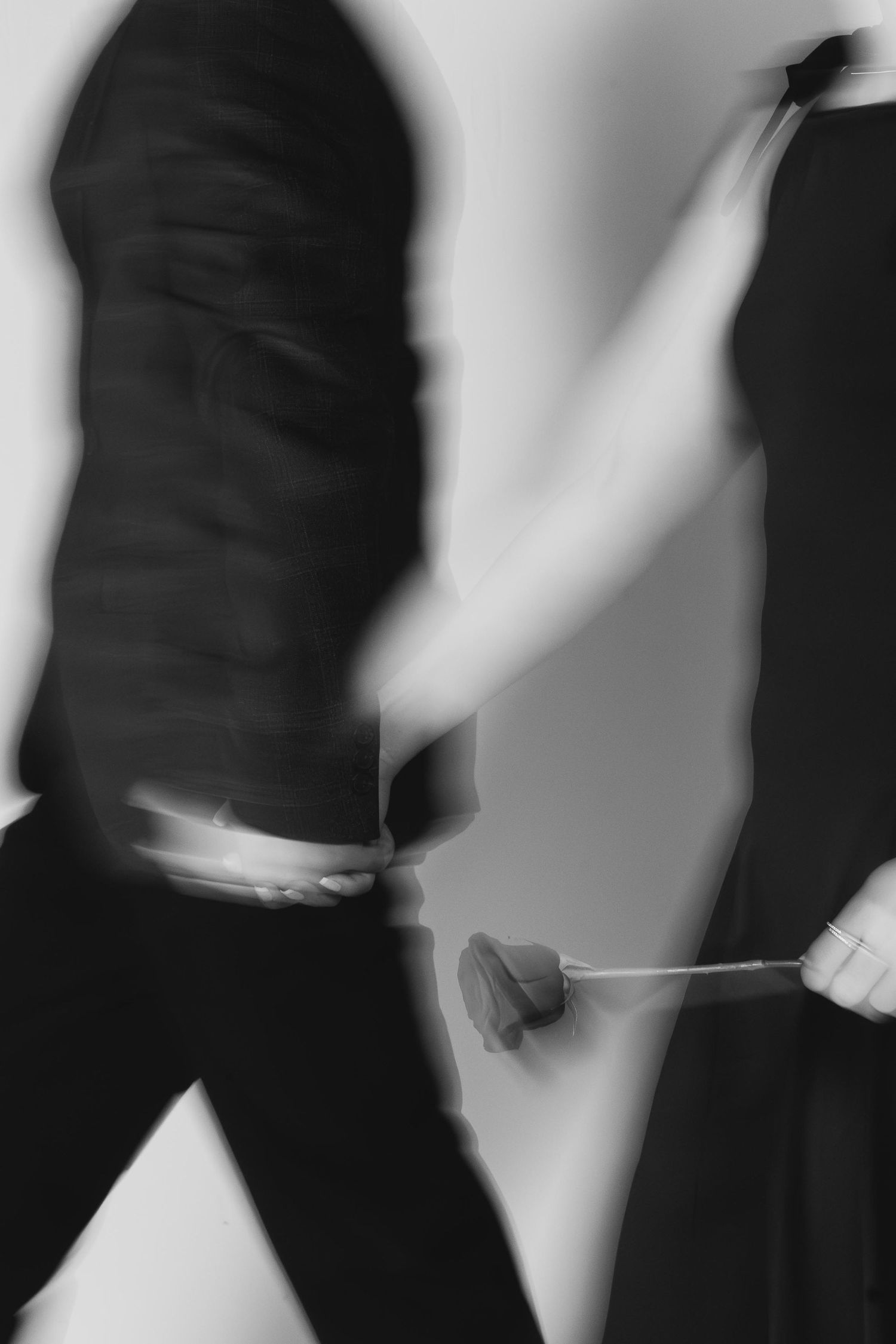 Blurred black and white photo of two figures in dark clothing, one holding a rose, captured with motion blur effect.