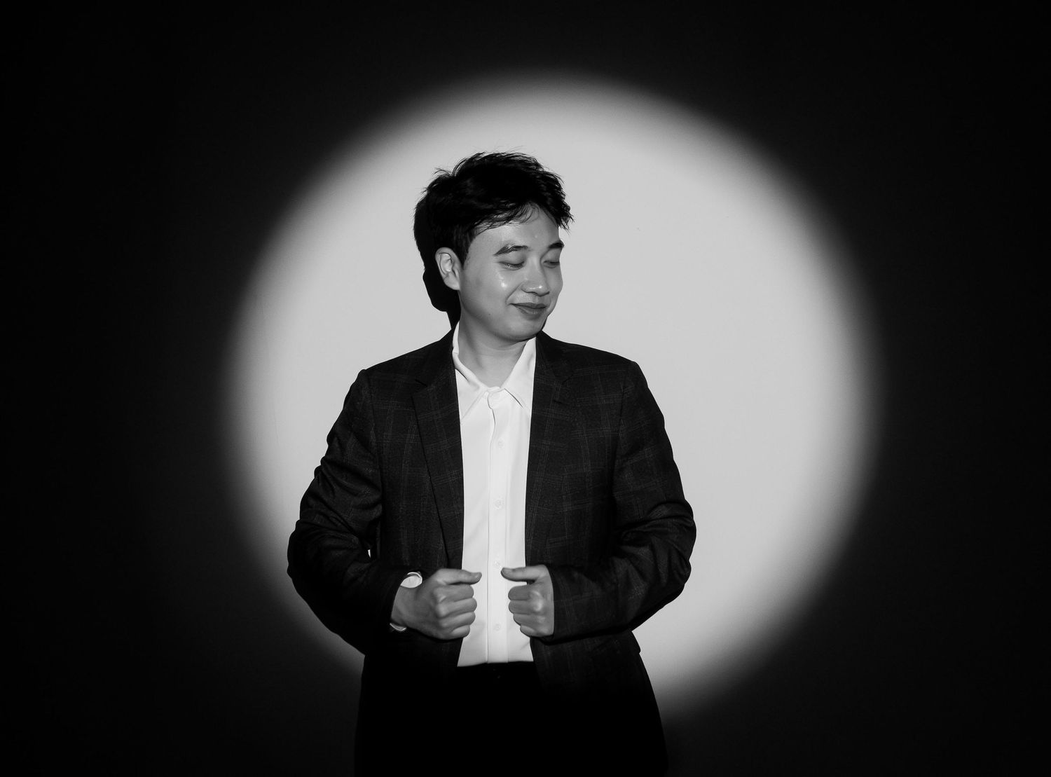 Young man in black blazer posing confidently in black and white spotlight portrait.