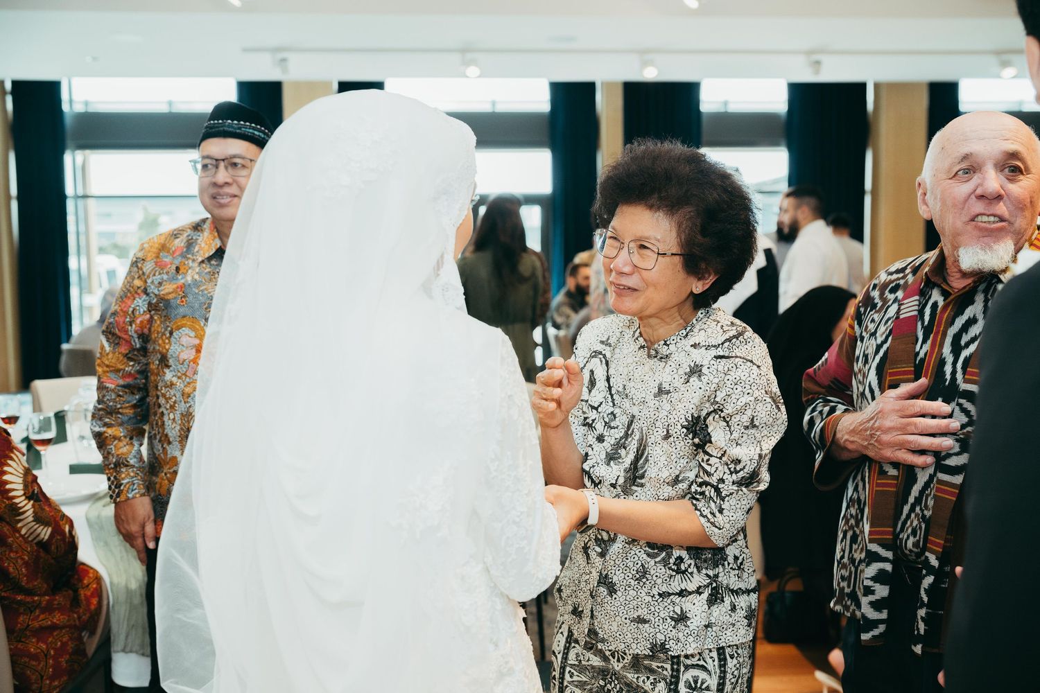 Wedding guests in traditional attire mingling and conversing at reception venue.