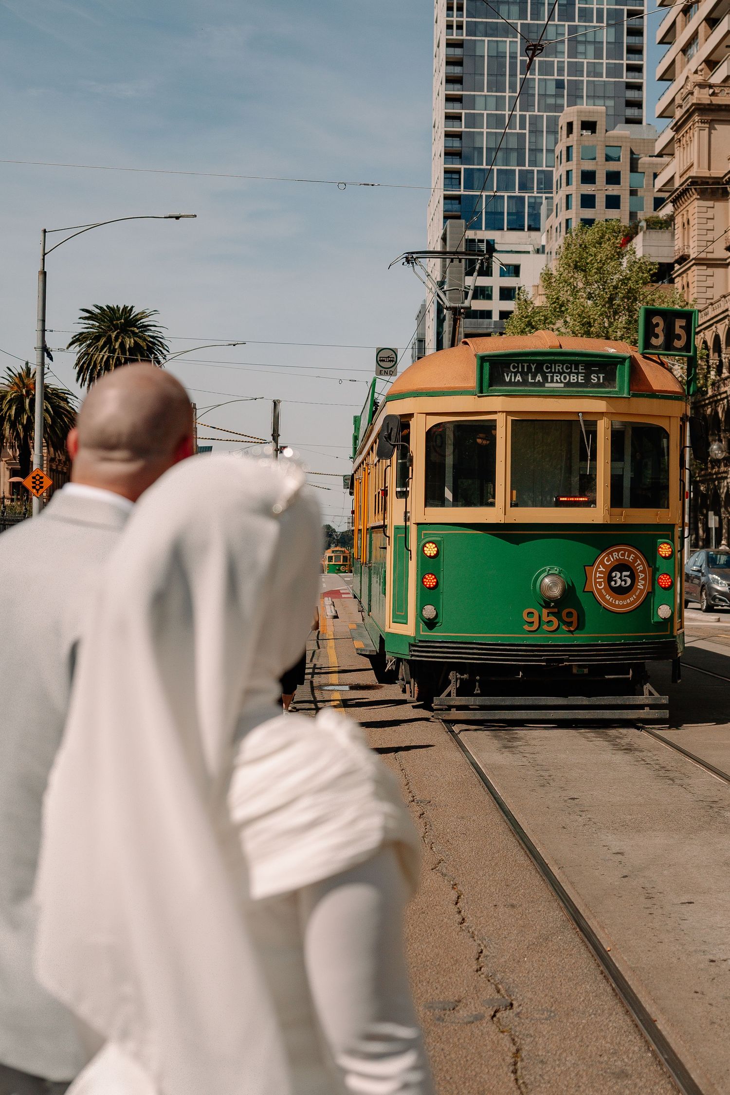 A man in white suit crosses street as a green City Circle tram number 35 approaches in Melbourne, Australia.