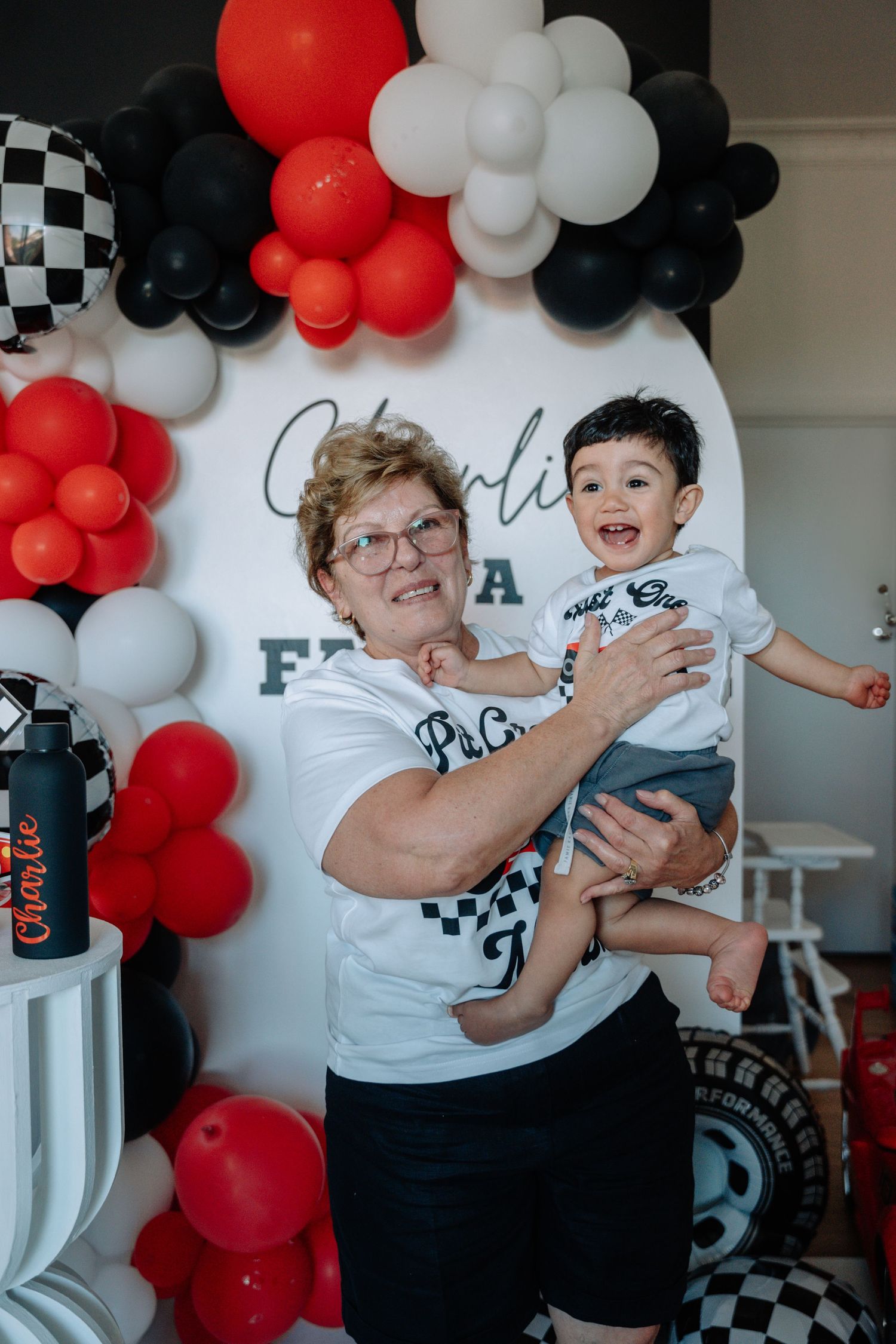 A joyful moment captured against a backdrop of red, white and black balloon decorations at a celebration event.