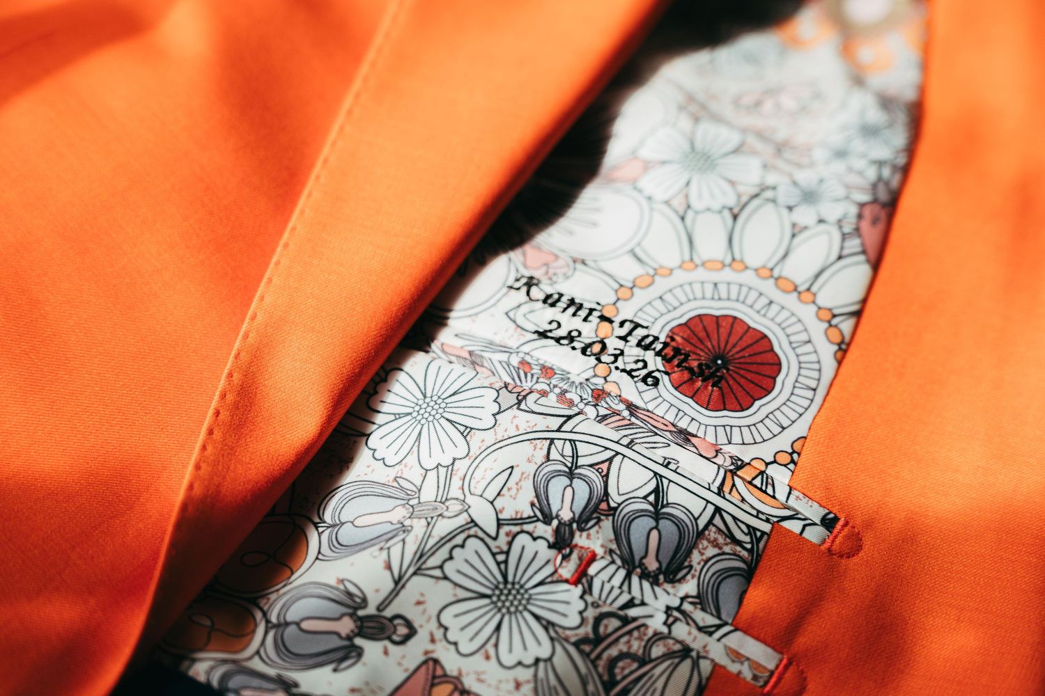 Close-up of an orange suit jacket lining featuring a floral pattern with a custom label.