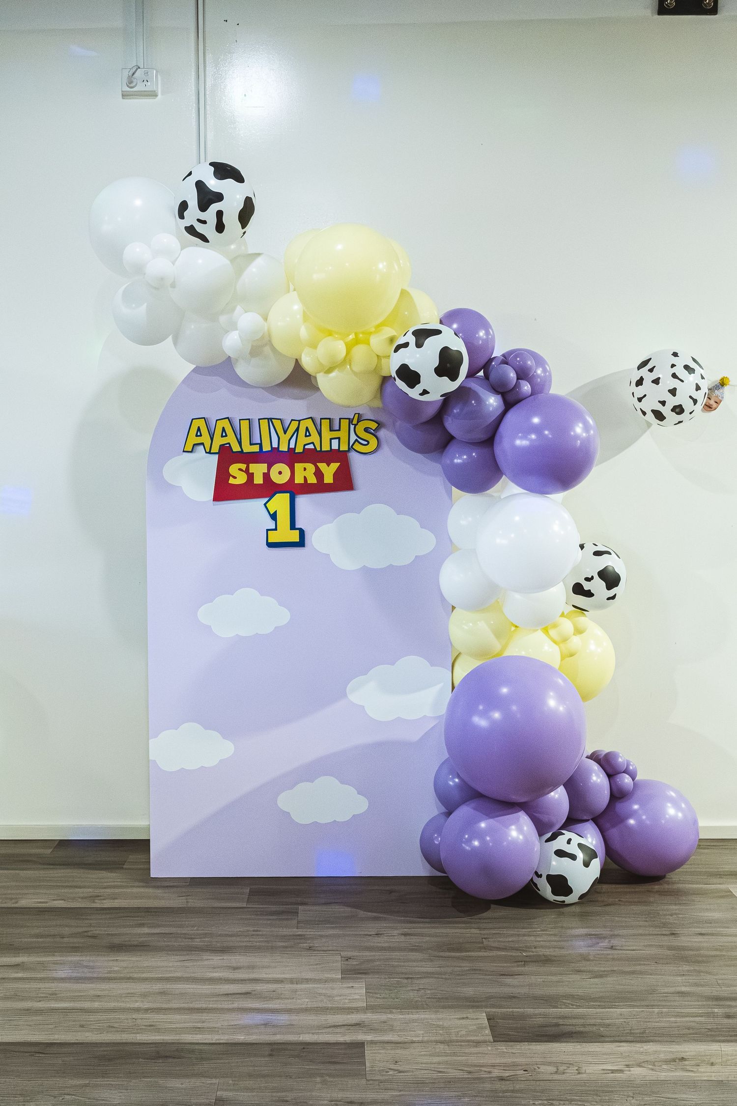 Toy Story themed party backdrop with purple, yellow and white balloon garland featuring cow print balloons and clouds.