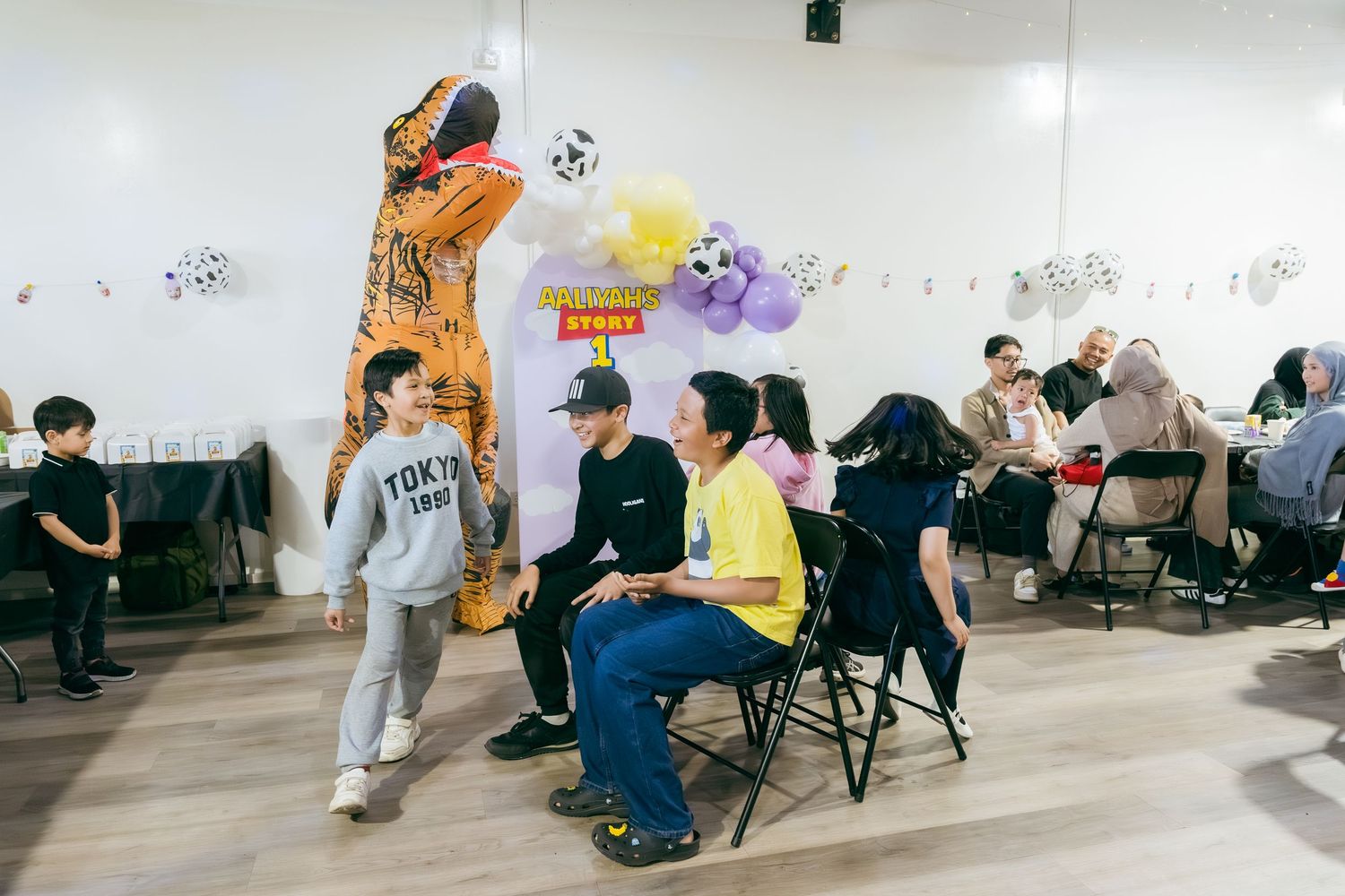 Students sit in chairs along a white wall decorated with colorful artwork during a classroom activity.
