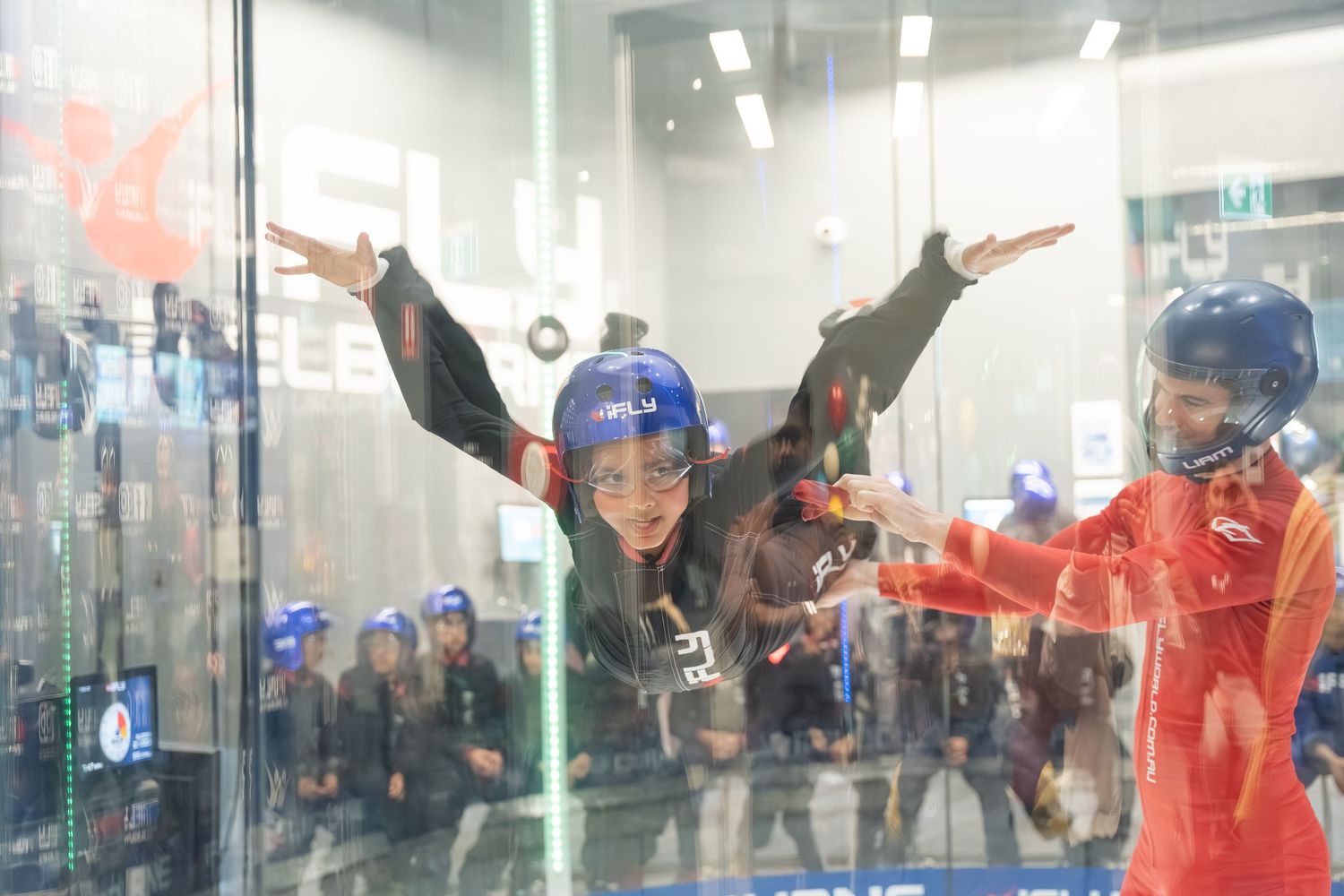 Indoor skydivers practice their flying skills in a vertical wind tunnel with instructors guiding them.