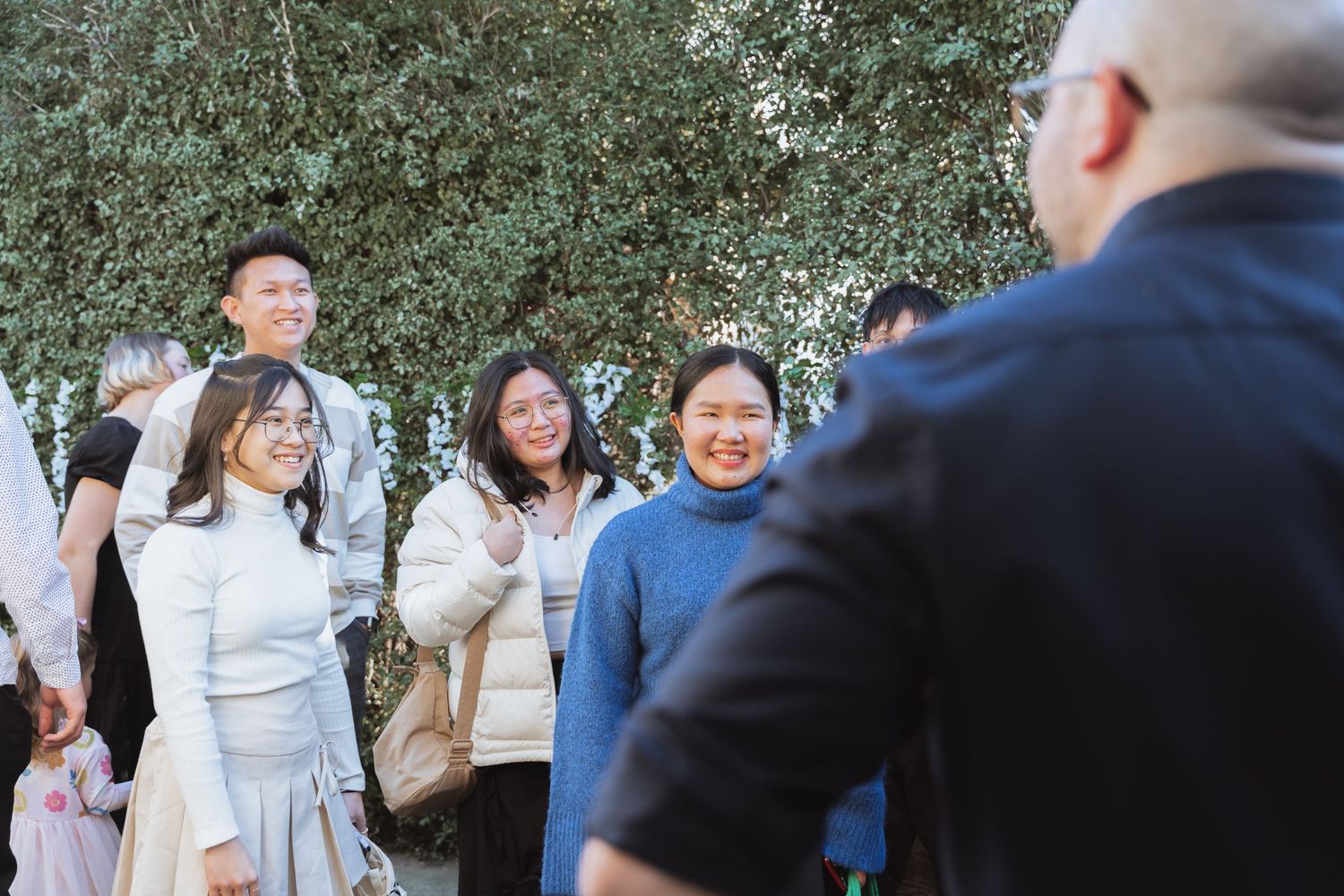 Guests mingling outdoors at a celebratory gathering with natural greenery in the background.