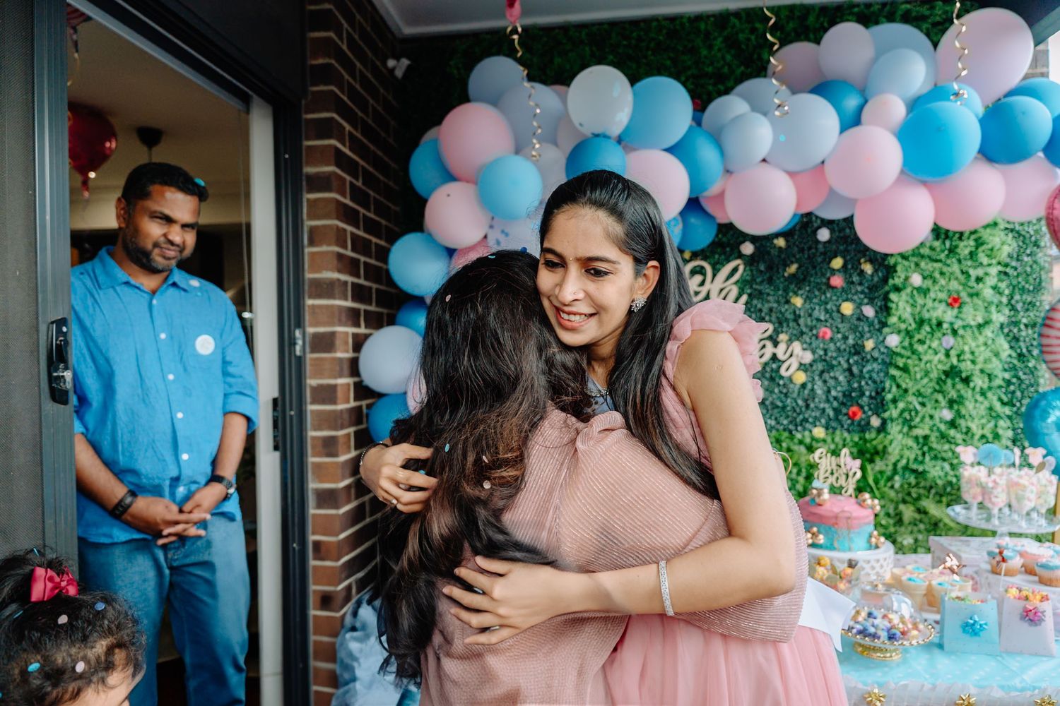 Pink and blue balloon arch decorates an outdoor gender reveal party setting.