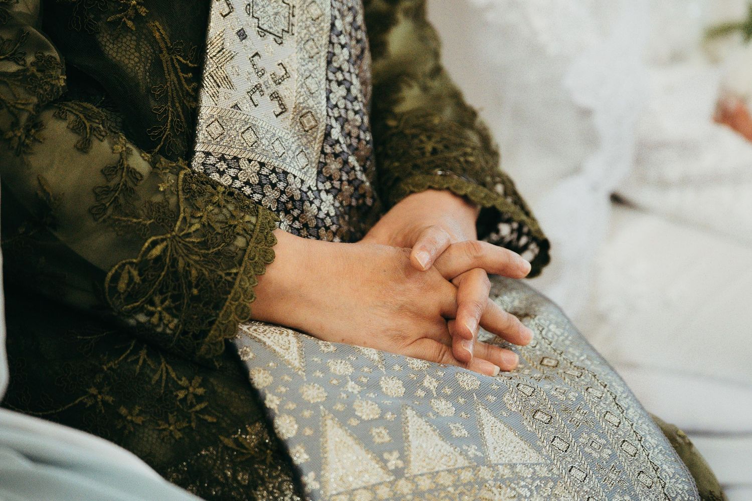 Close-up of groom hands clasped in ornate dark green embroidered wedding attire.