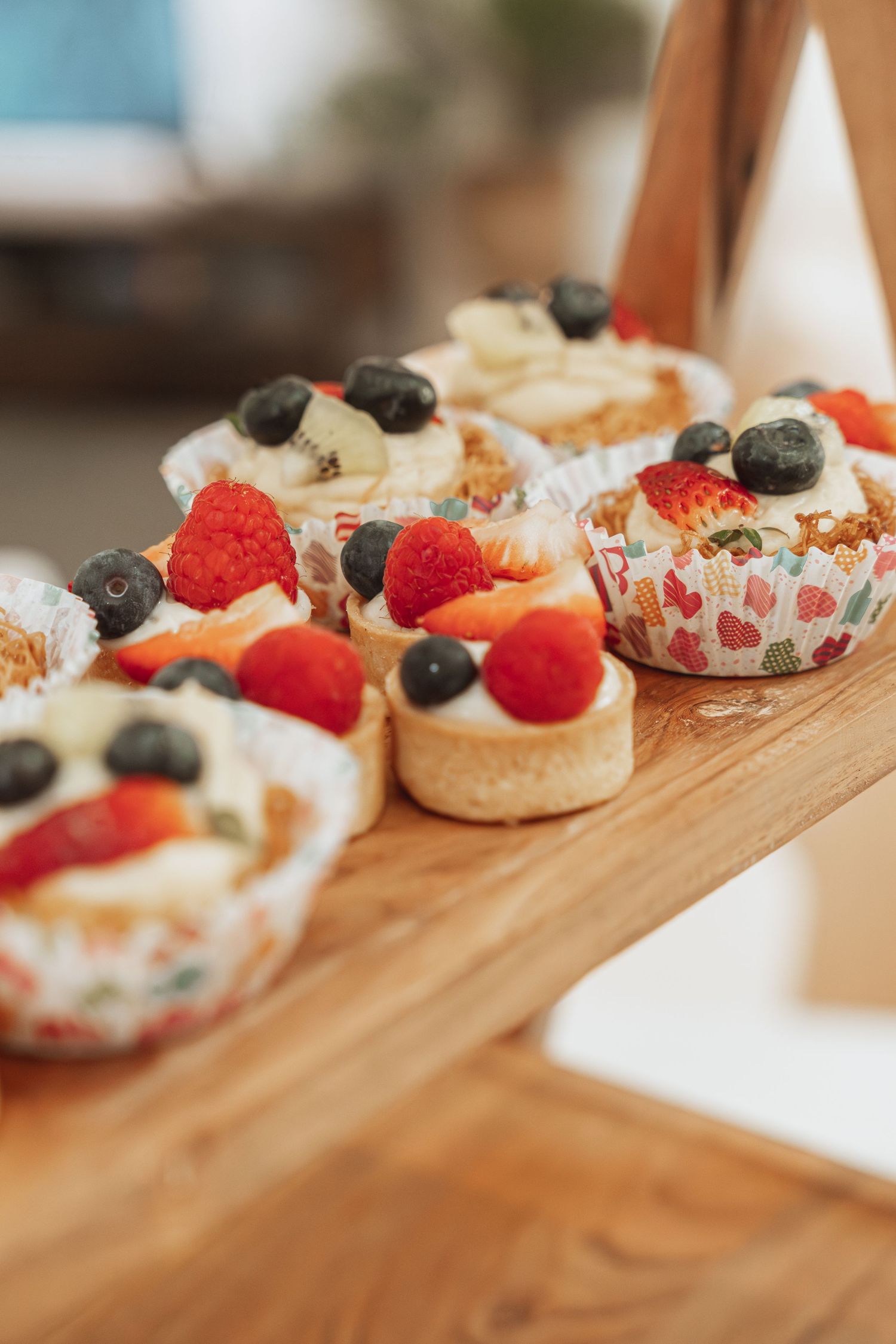 Mini fruit tarts with fresh berries and cream arranged in a line on a wooden serving board.