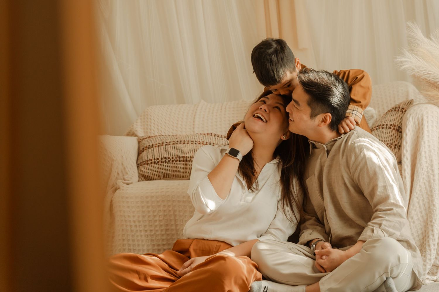 Couple in white clothing embraces intimately on couch in warm-toned living room setting.