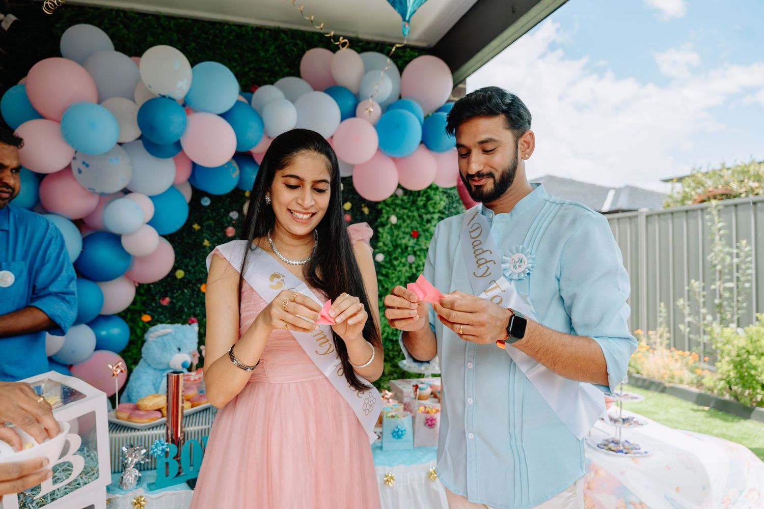 Outdoor celebration with pink and blue balloon decorations under covered patio.