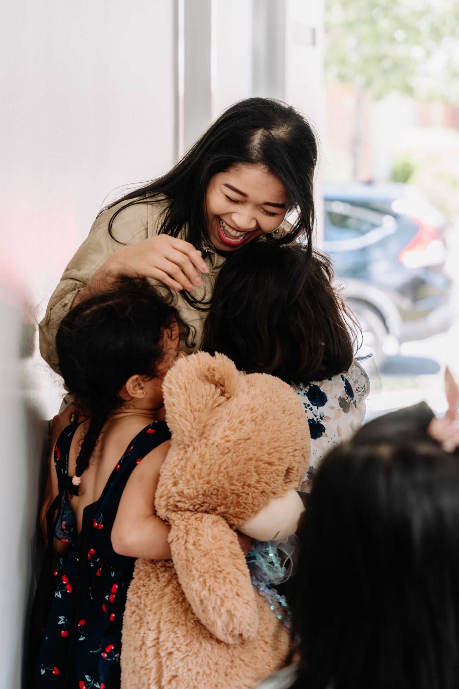 A person in a dark floral dress hugs and plays with a large tan teddy bear in a series of candid shots.
