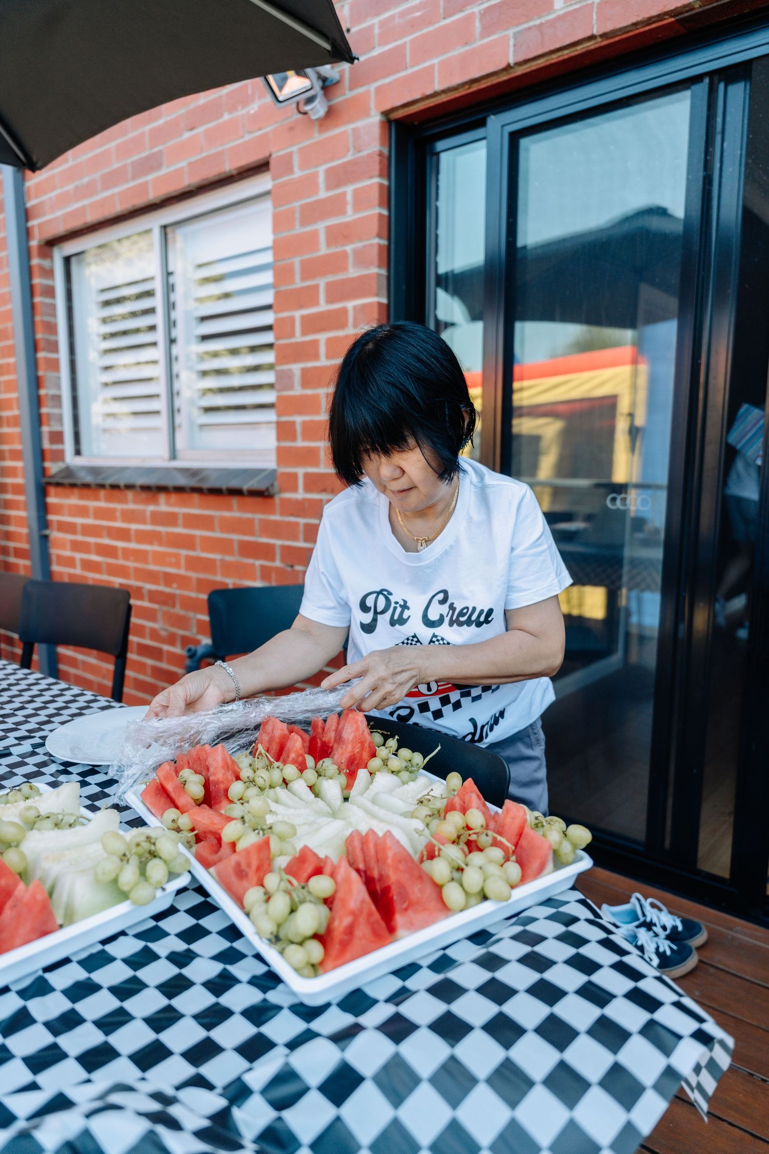 Person arranging fresh fruit platters on a checkered tablecloth outdoors.