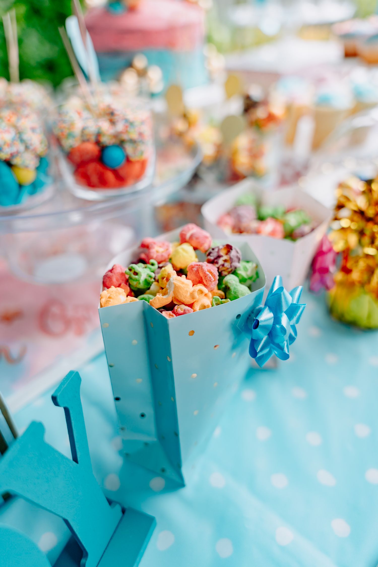 Colorful popcorn treats served in turquoise blue gift boxes with decorative bows at a festive party setup.