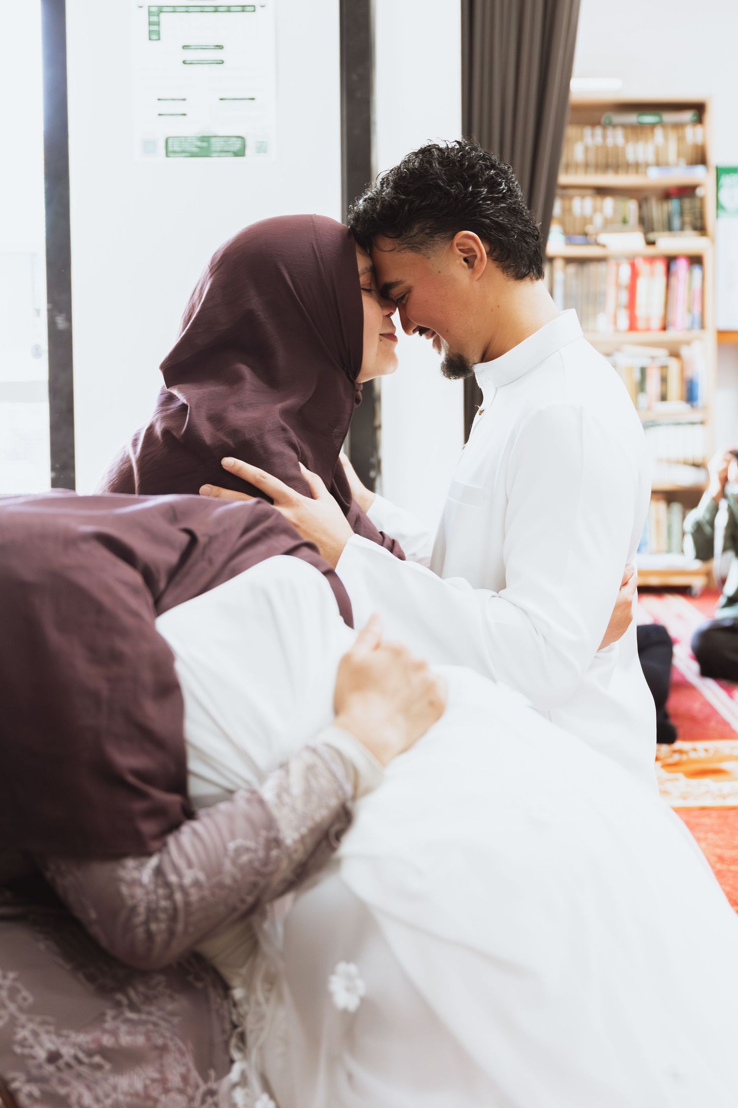 Muslim couple sharing a tender forehead touch moment during a traditional Islamic ceremony indoors.