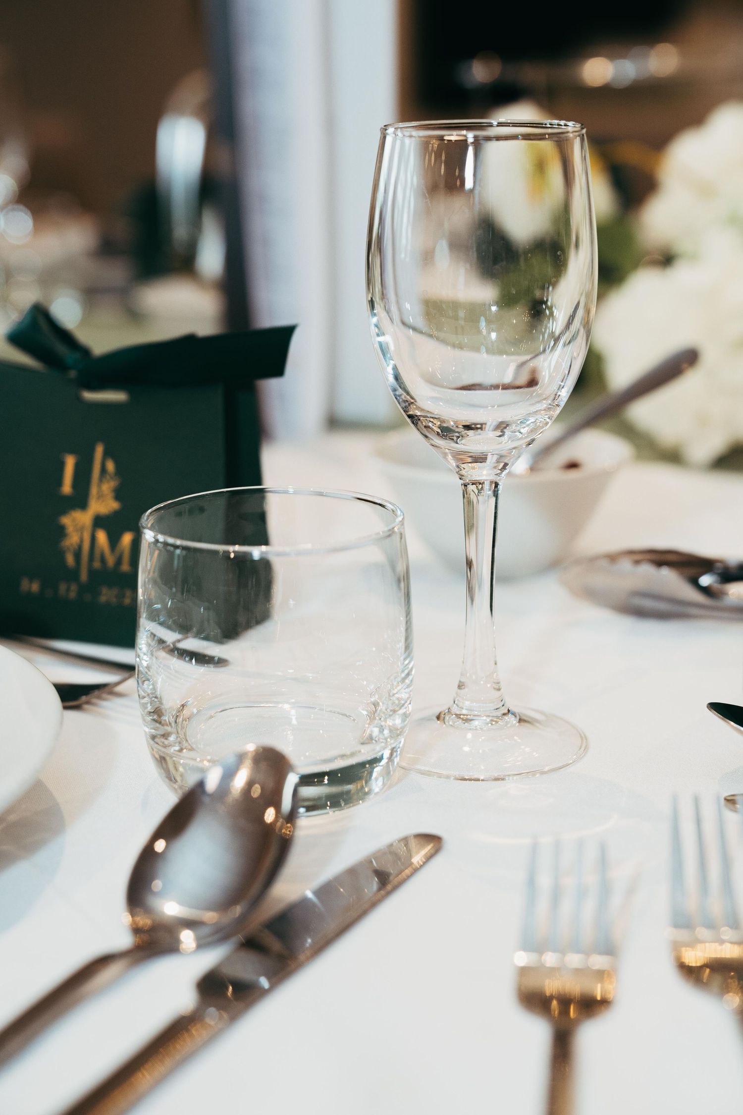 Elegant wedding reception table setting with crystal wine glass and gold monogram gift box.