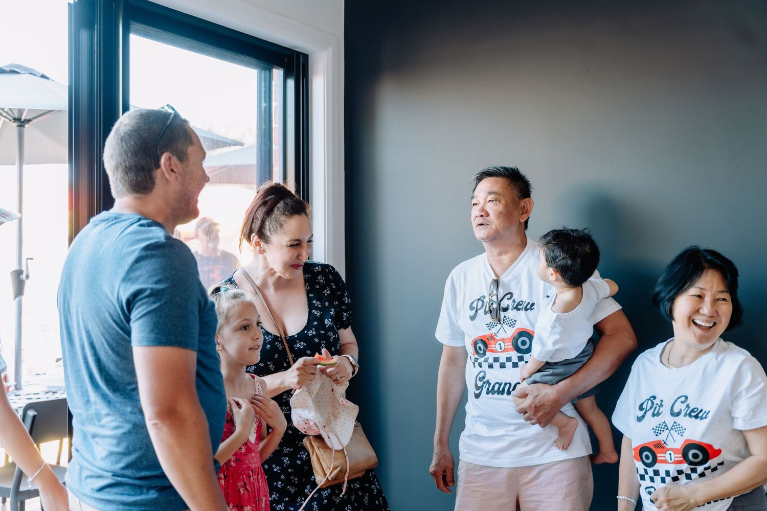 Family gathering in a bright room celebrating a special occasion with joyful expressions.