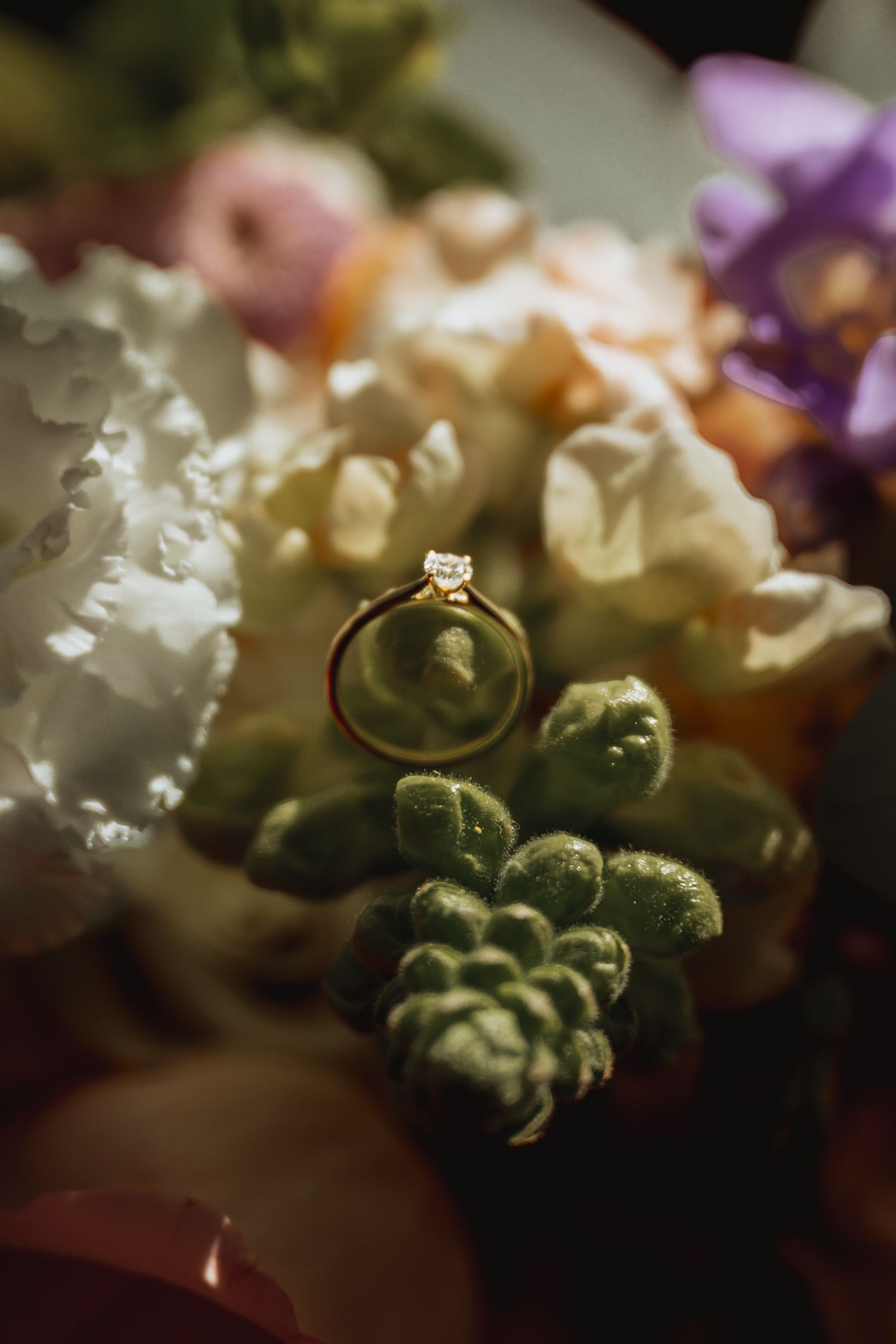 Close-up macro shot of wedding rings nestled among delicate white and purple flowers.