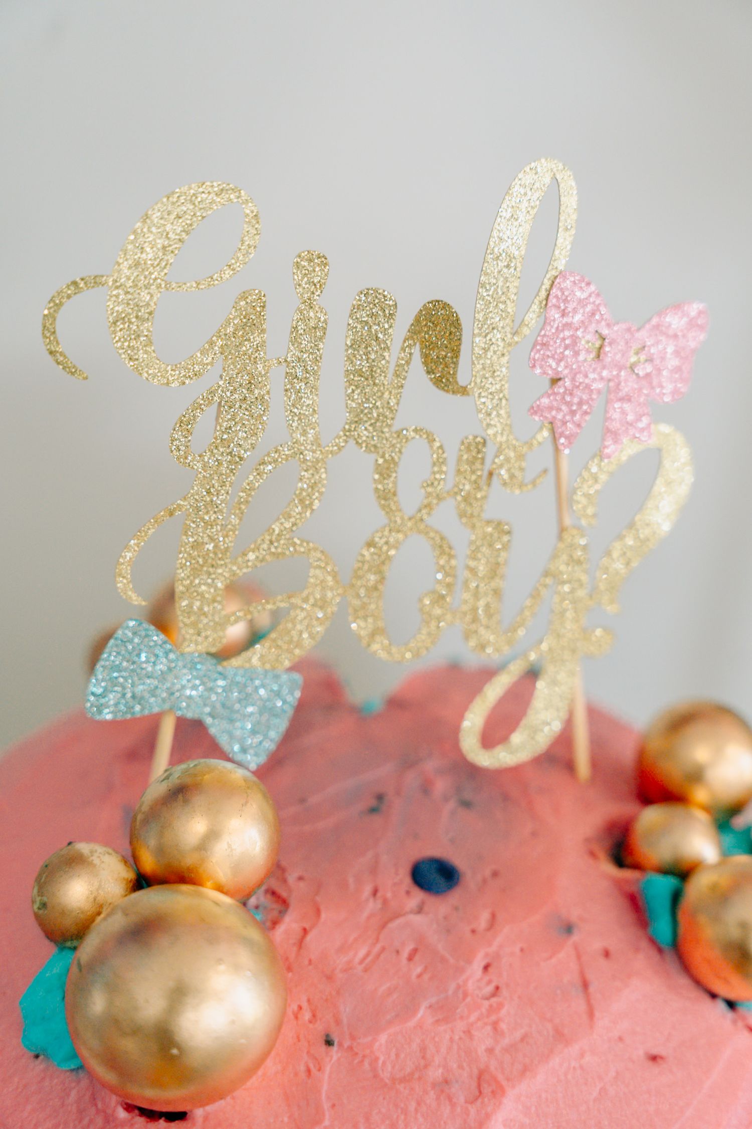 Gold glitter cake topper decorations with pink accents against a gray background.