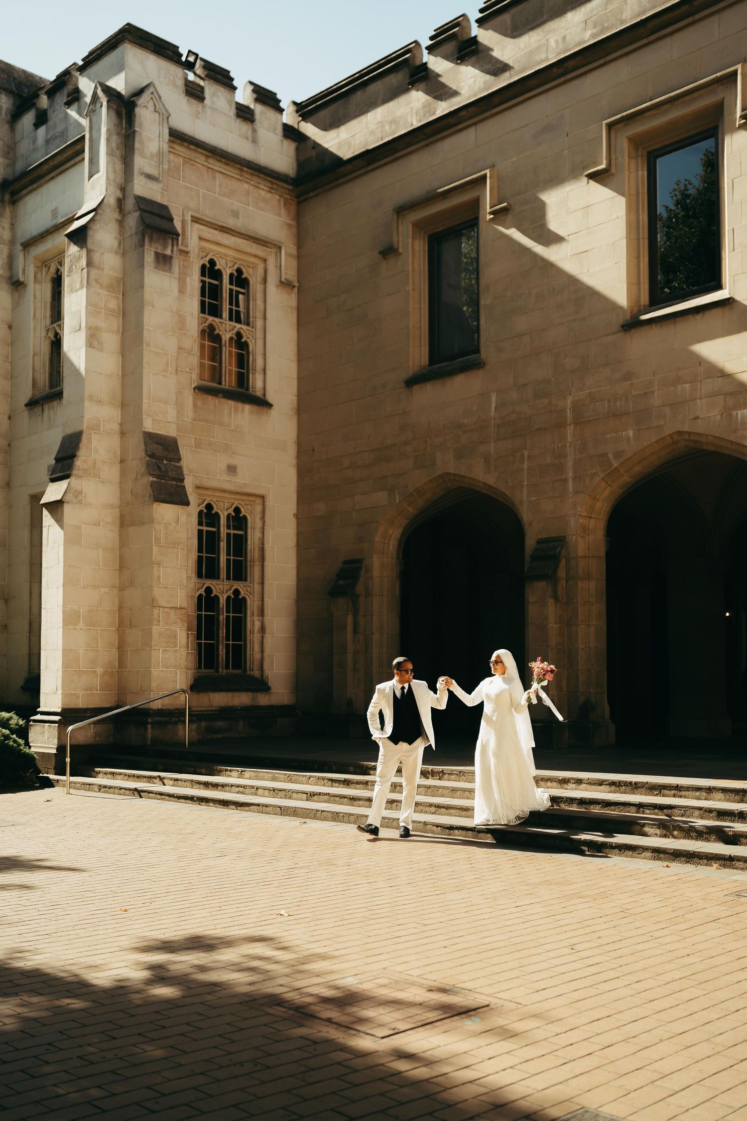 Bride and groom holding hands outside a historic stone castle venue on their wedding day.