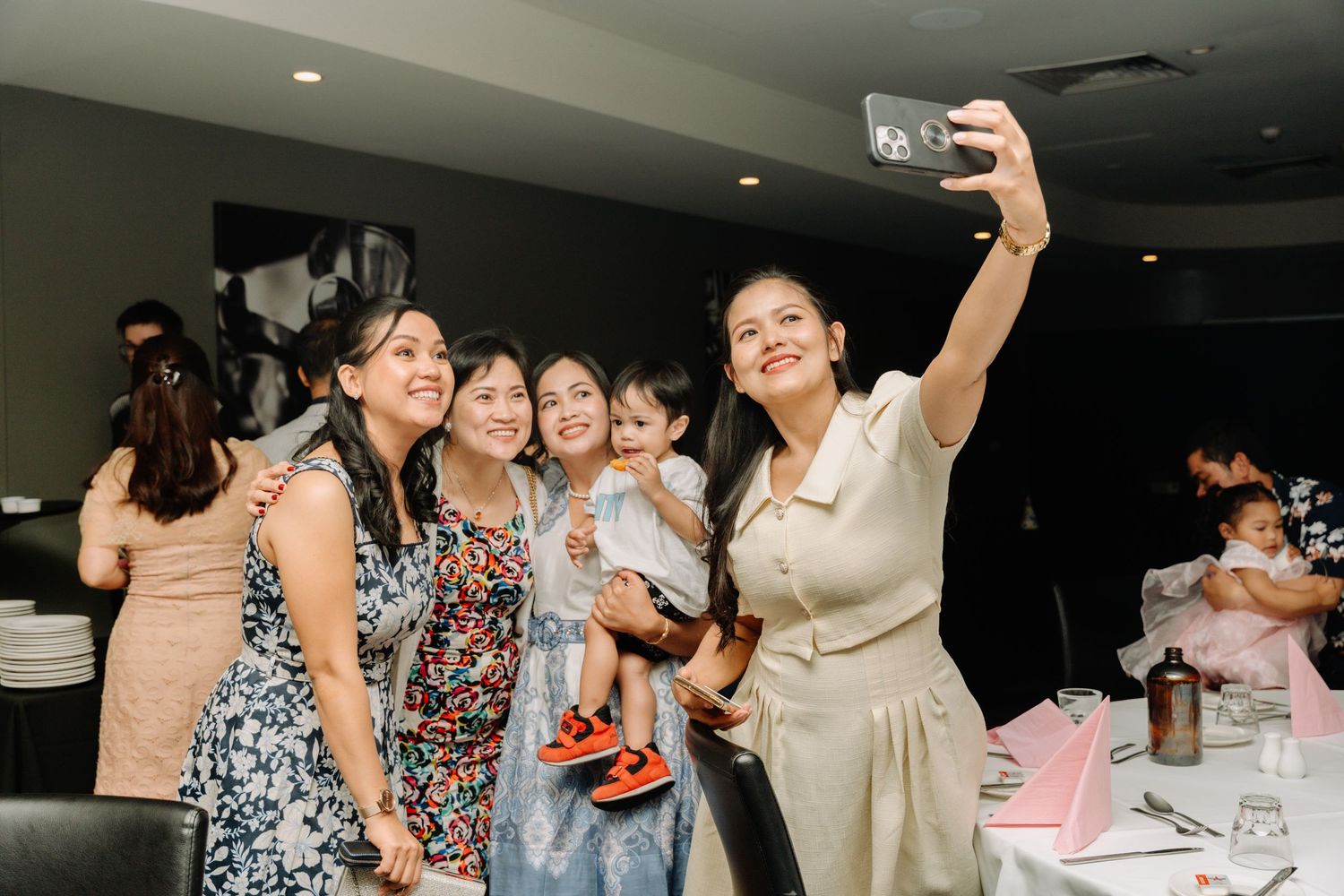 Friends taking a group selfie at a party decorated with balloons and tables.