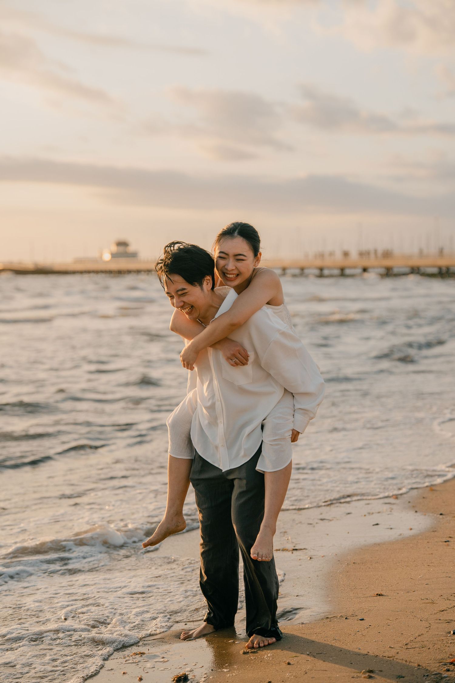 Man giving woman a piggyback ride on the beach at sunset.
