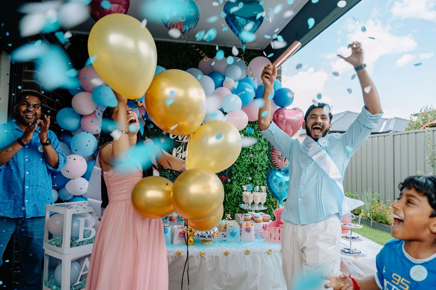 Festive outdoor party celebration with gold and blue balloons, decorative table setup and joyful guests celebrating.