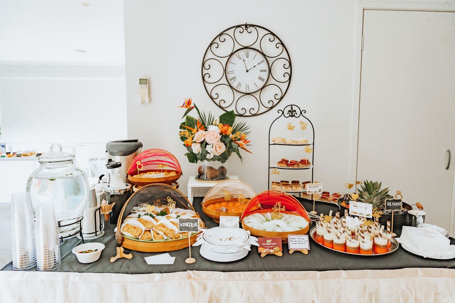 Elegant dessert and refreshment table display with cakes, flowers and decorative clocks at a special event.