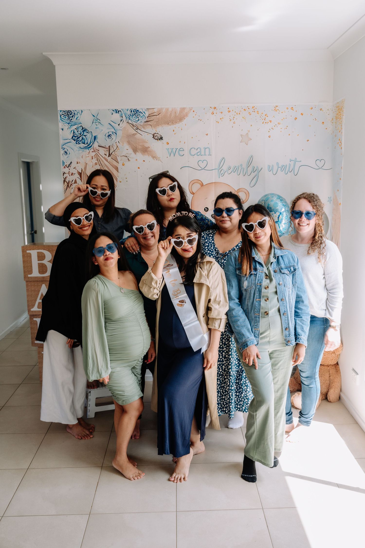 Group wearing matching blue sunglasses pose together against a white wall with decorative text.