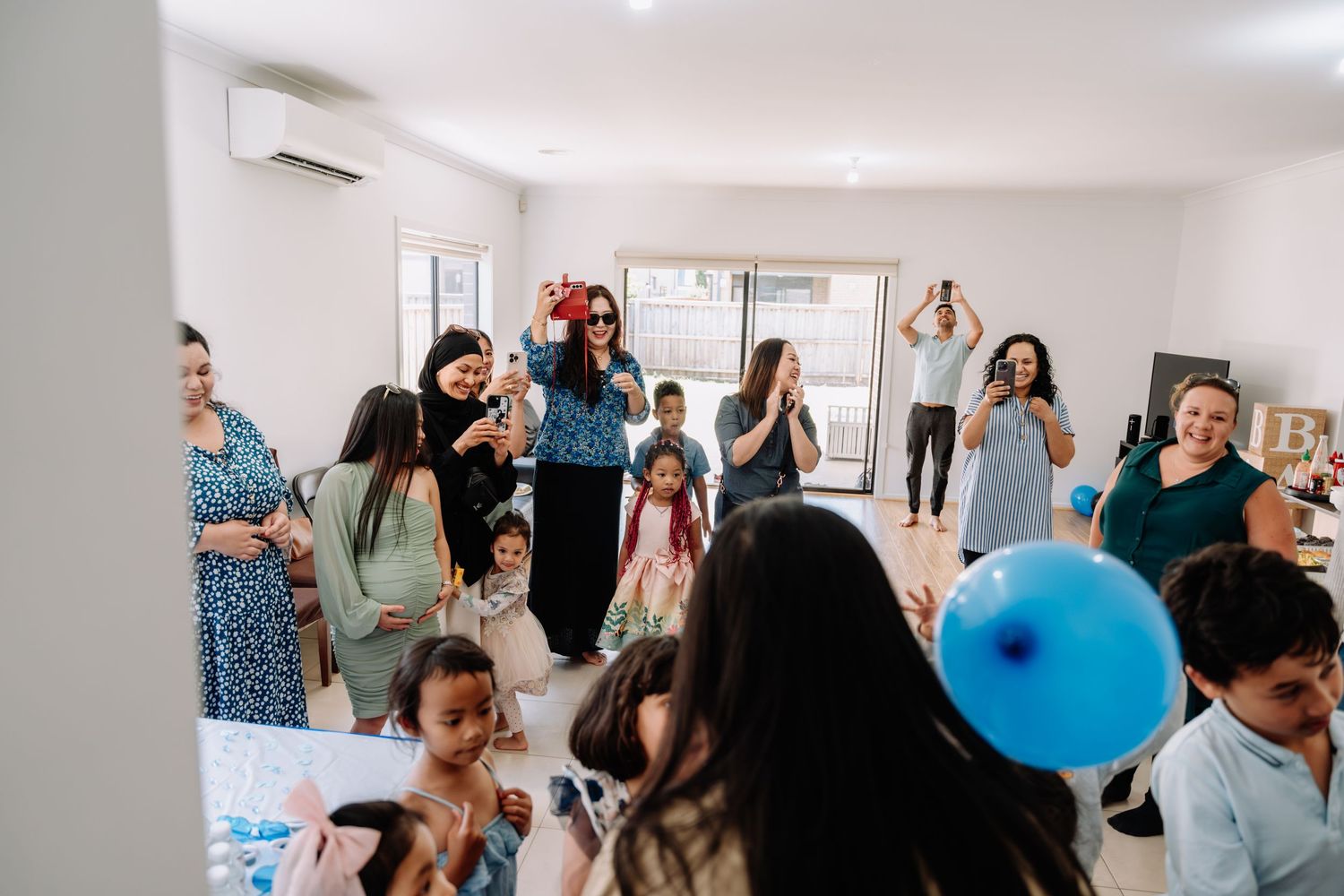 A lively indoor party scene with people gathered in a bright room, with a blue balloon visible among the crowd.