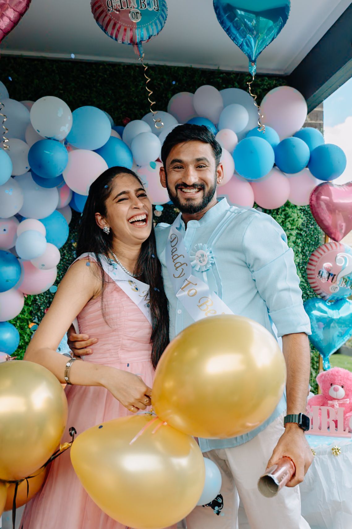 Festive gender reveal party with gold and pastel balloon decorations in an indoor setting.