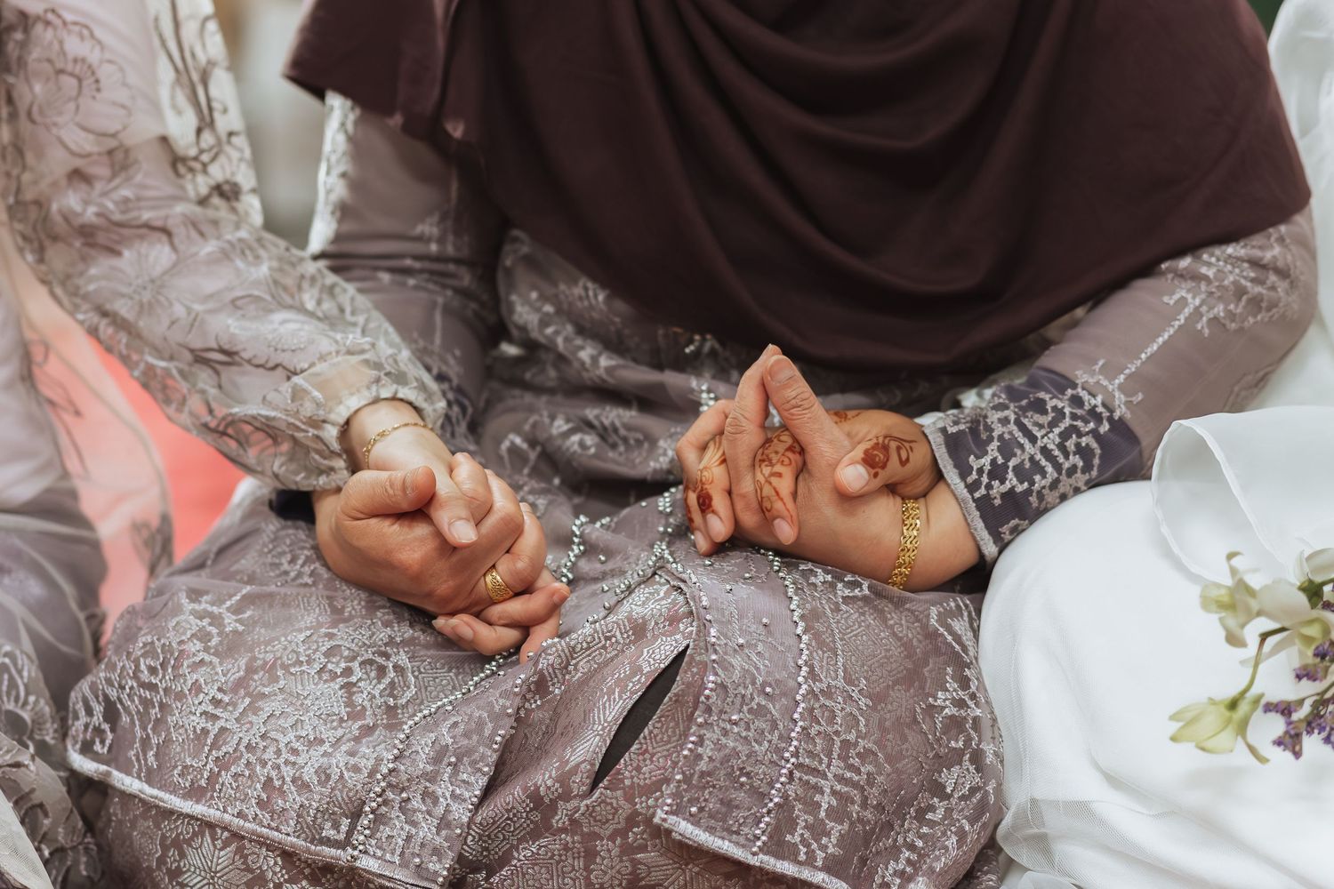 Two women in traditional Islamic attire holding hands, adorned with henna and gold bracelets, during a cultural ceremony.