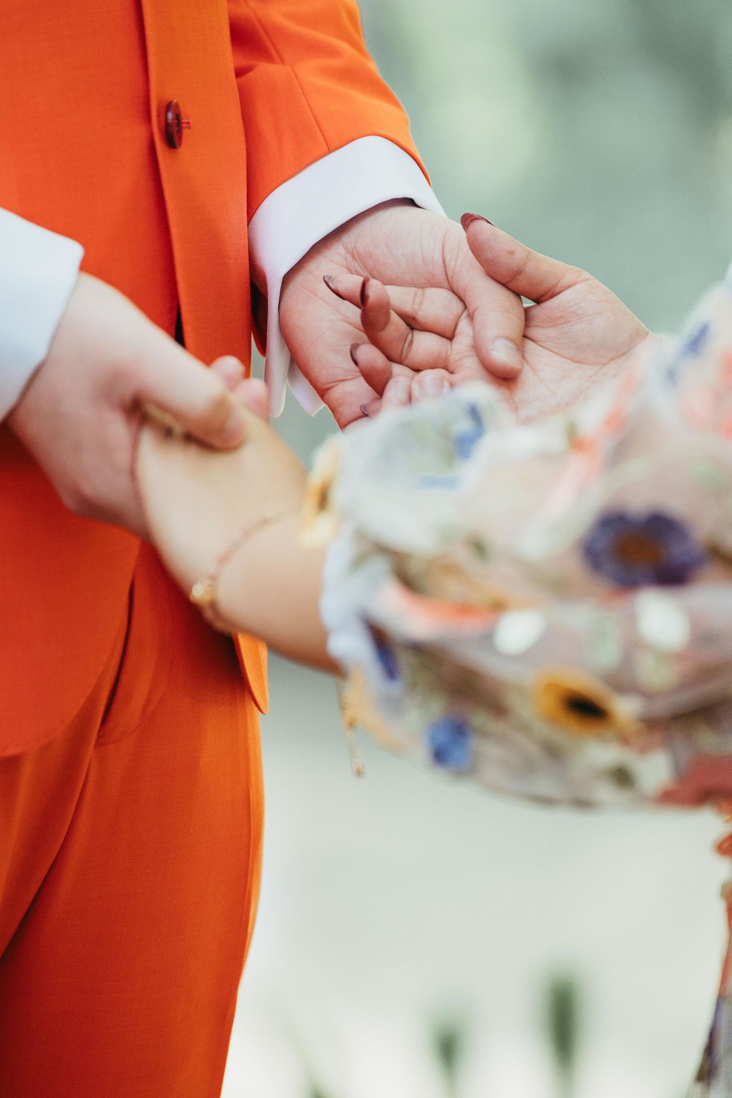 Groom in orange suit exchanging rings with bride holding a colorful floral bouquet.