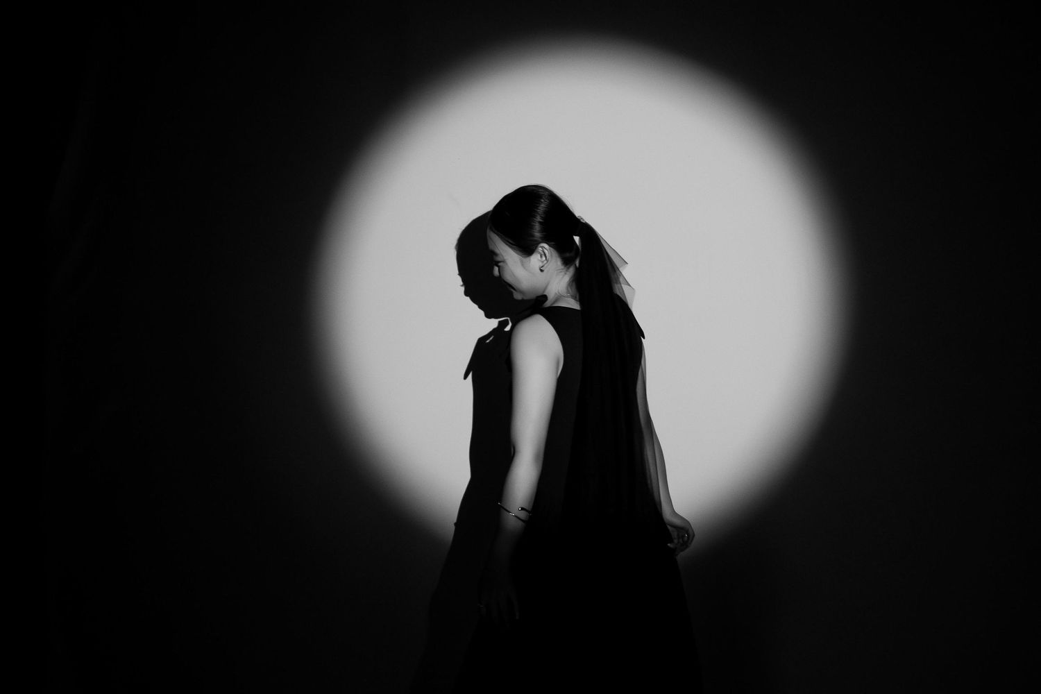 Black and white silhouette of a woman in a dress posed against a glowing spotlight backdrop.