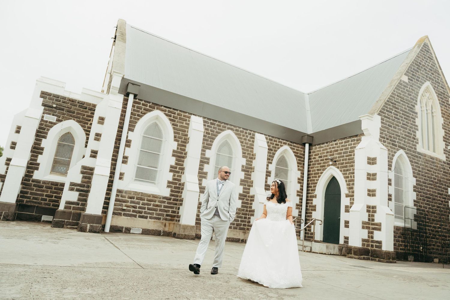 Bride and groom holding hands outside a historic stone church on their wedding day.
