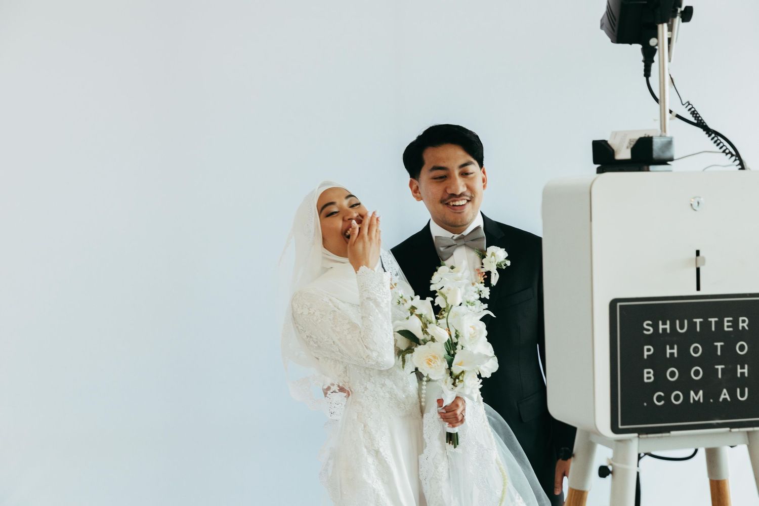 A smiling Muslim bride and groom pose together at a photo booth at their wedding reception.
