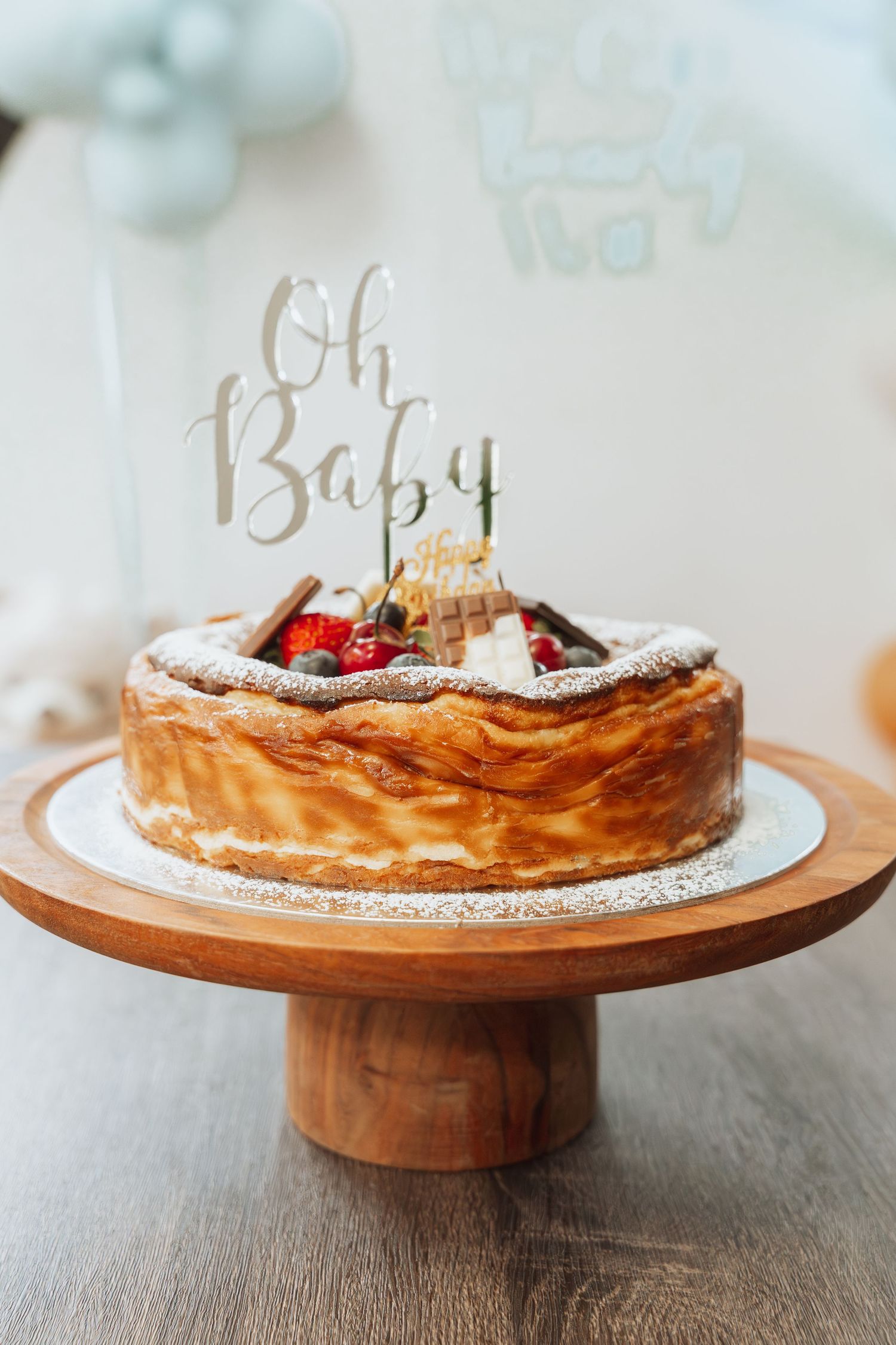 A rustic baby shower cake with 'Oh Baby' topper and fresh berries on a wooden cake stand.