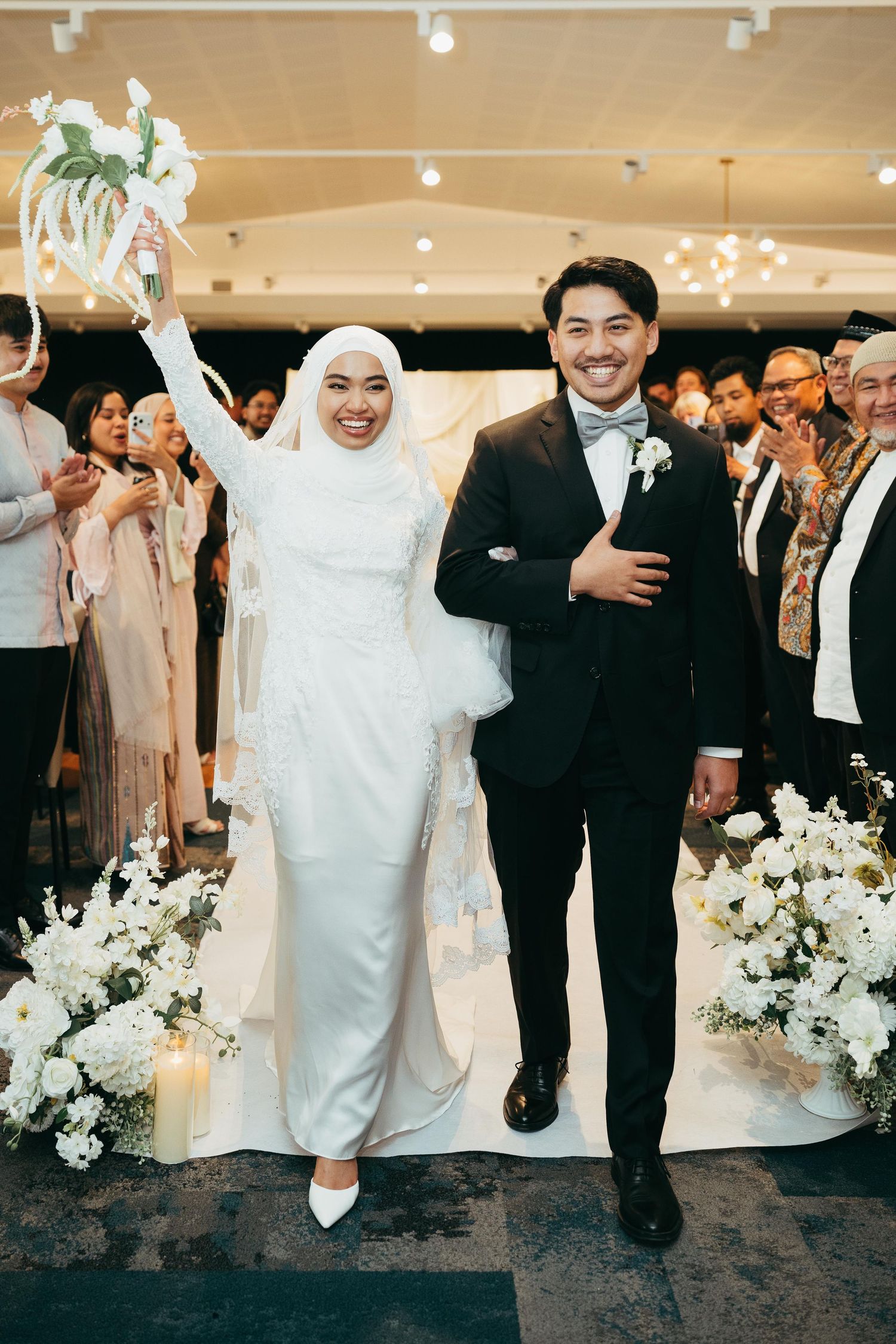 Joyful newlyweds walking down aisle at elegant white floral wedding reception.