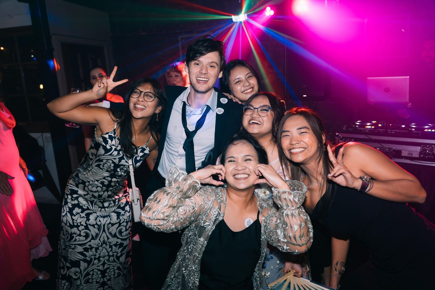 Group of friends dancing and posing under colorful disco lights at a lively wedding reception.