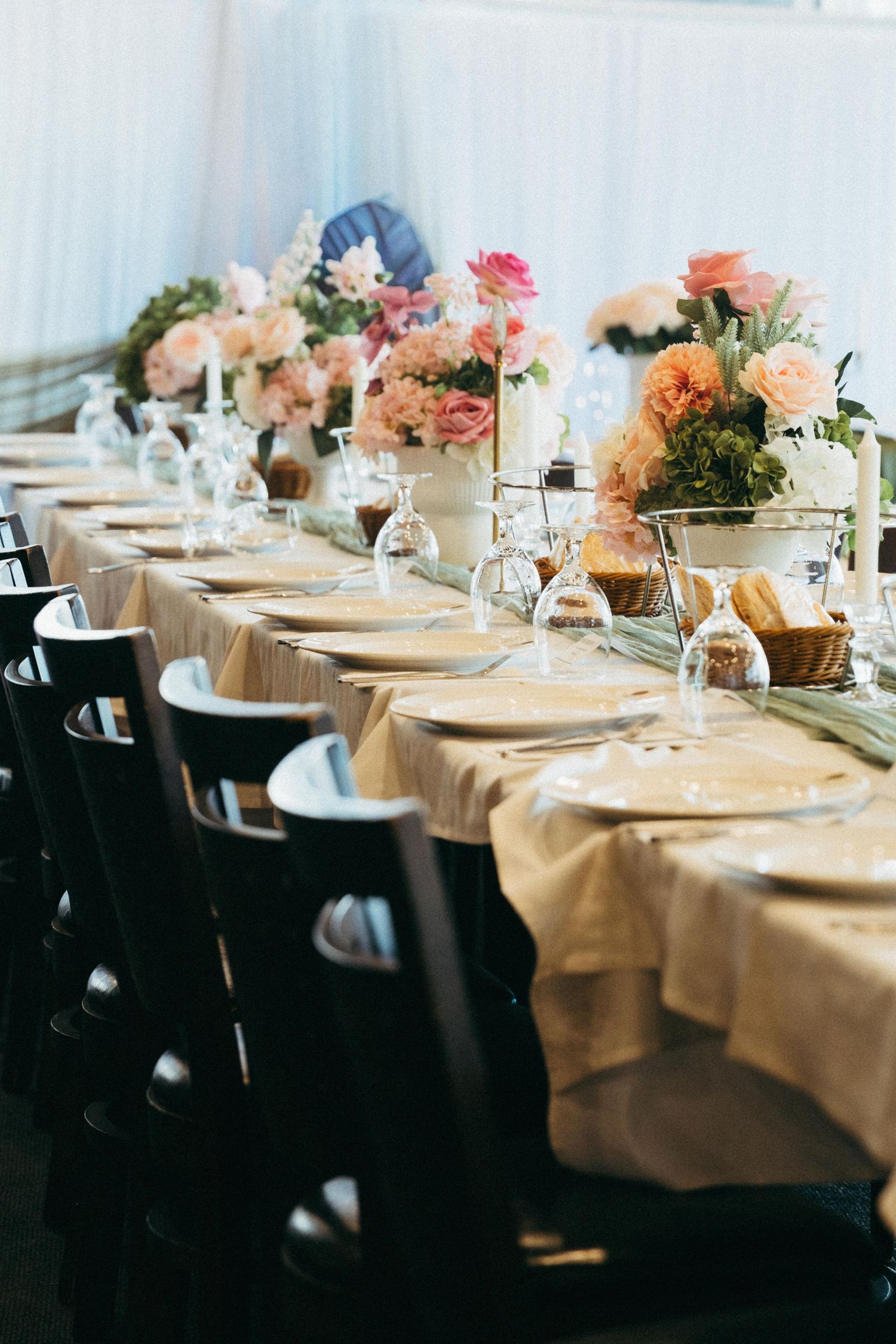 Elegant wedding reception long table with gold linen, crystal glasses, and pink floral centerpieces under a white tent.