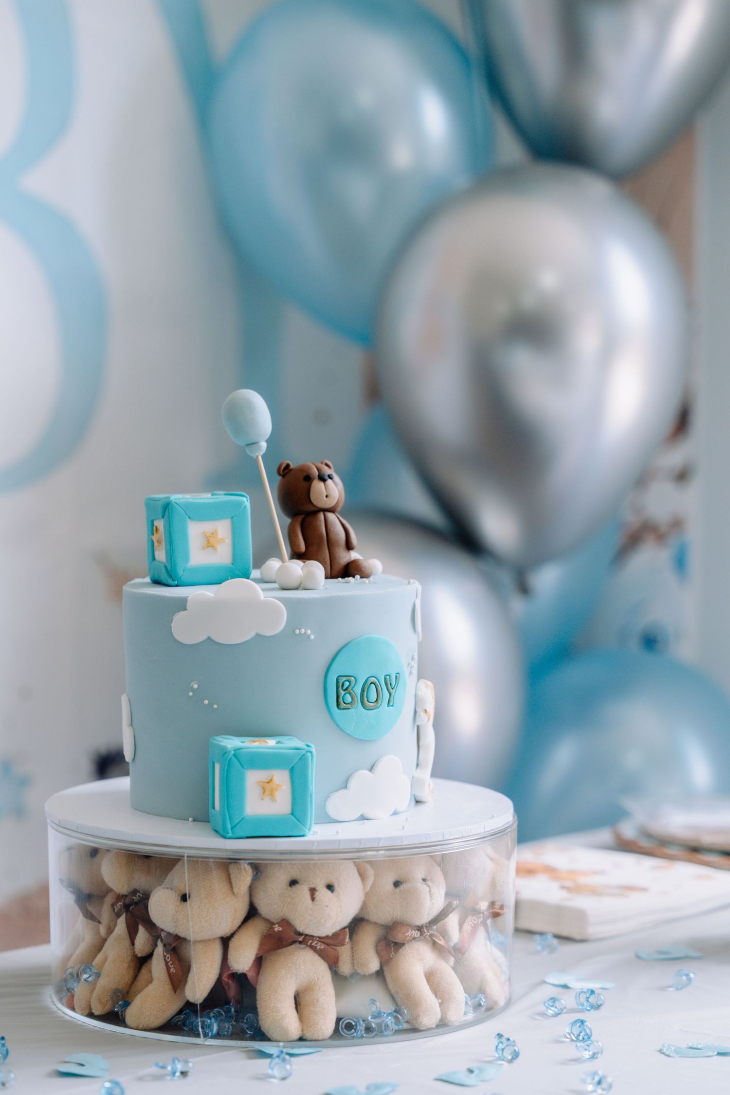 Light blue baby boy cake with white clouds and plush teddy bears arranged around the base.